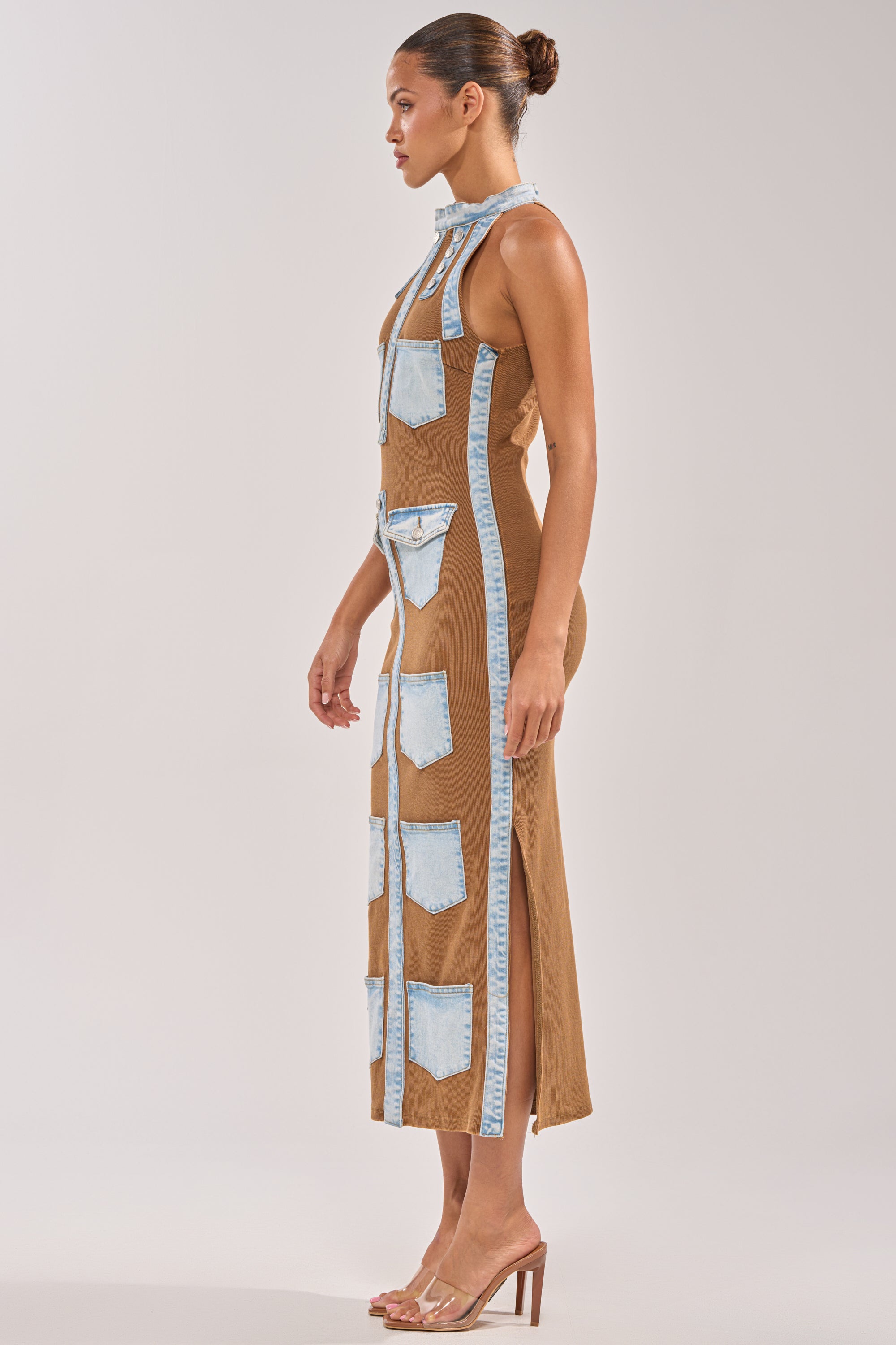 A woman in profile wears the POCKET THEORY PATCHED UP MAXI, a sleeveless brown bodycon dress with light blue denim pocket details, styled with a bun and clear high-heeled sandals against a plain background. 2