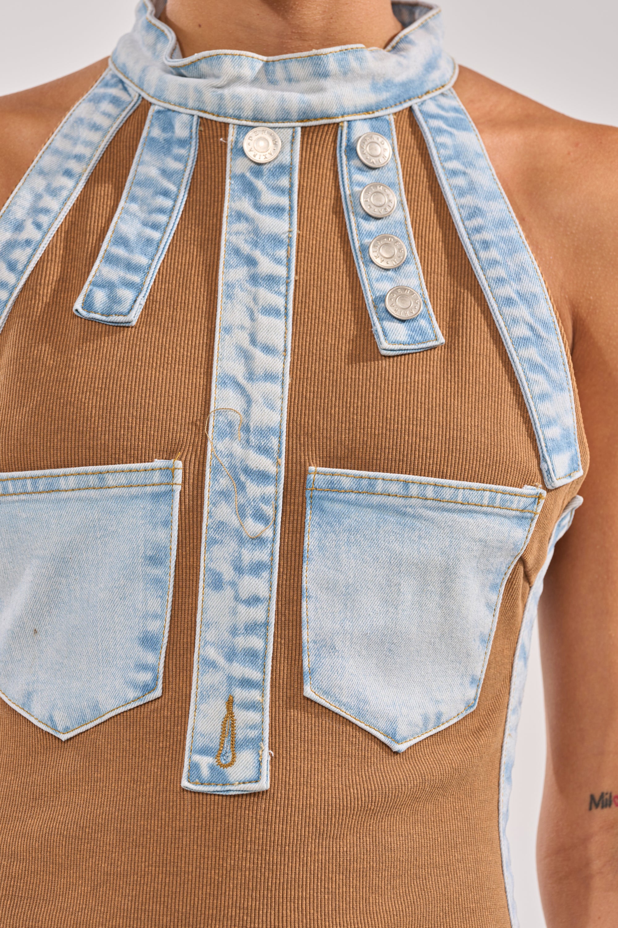 Close-up of the POCKET THEORY PATCHED UP MAXI, a brown ribbed top featuring denim pocket detailing, two front pockets, vertical stripes, decorative silver buttons, and a high collar. 5