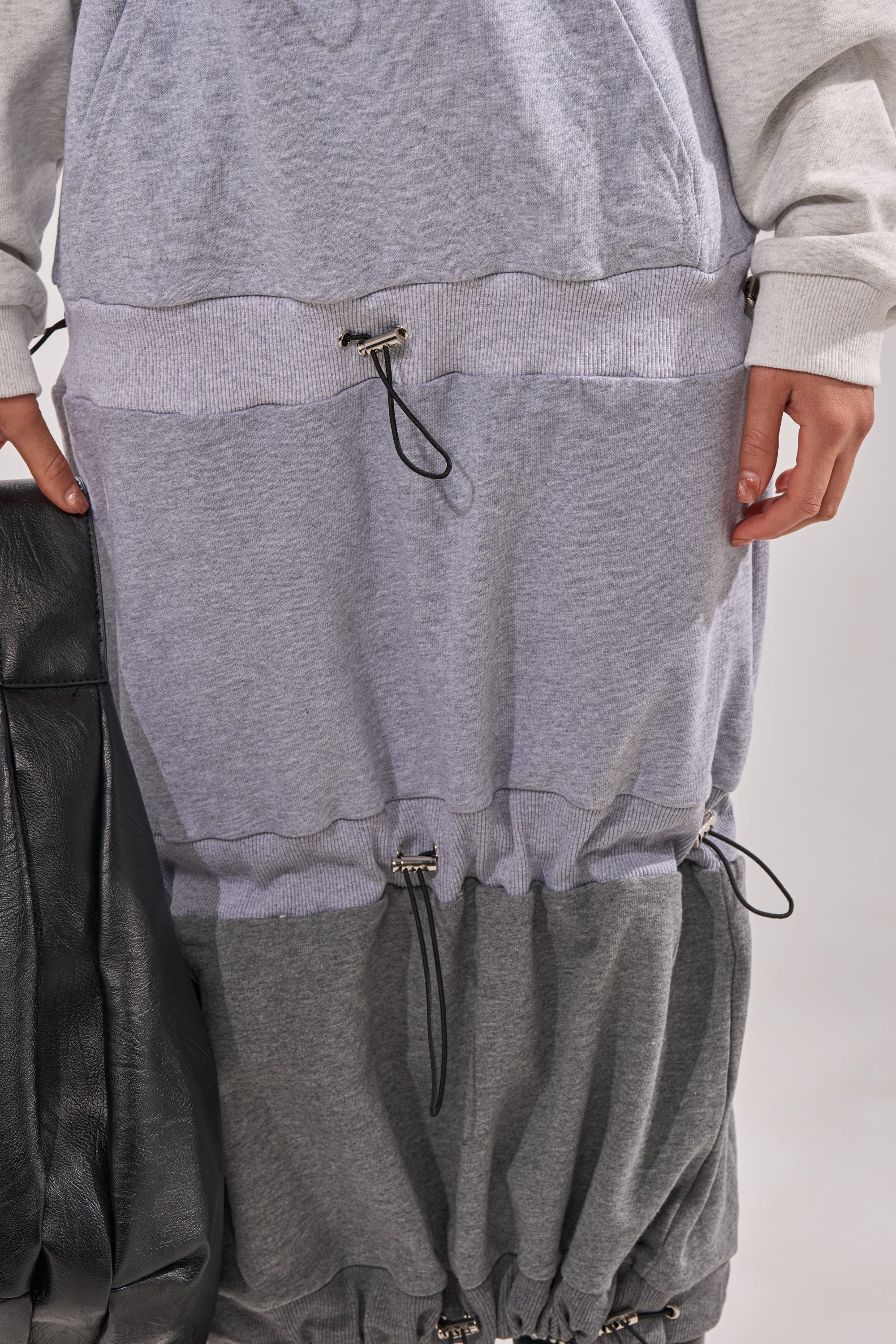 Wearing the TIED UP RIGHT NOW MAXI DRESS with adjustable drawstrings, someone holds a large black bag. Only the lower torso, hip, and hand are shown, highlighting the dress’s colorblock streetwear style. 5