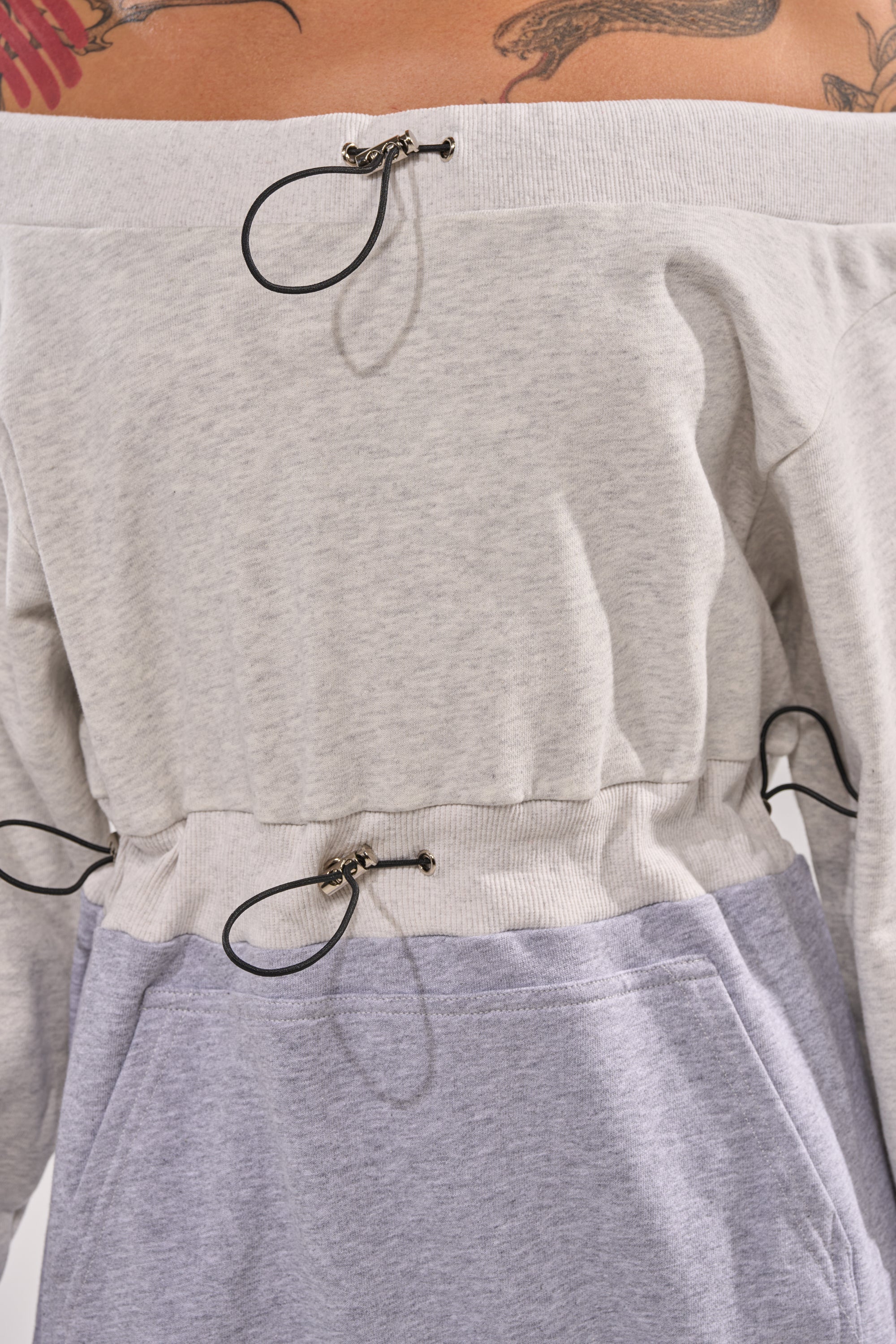 A close-up of a person wearing the TIED UP RIGHT NOW MAXI DRESS, featuring a colorblock design, off-shoulder neckline, and adjustable black drawstrings at the waist. Part of a colorful tattoo is visible on their upper chest. 6