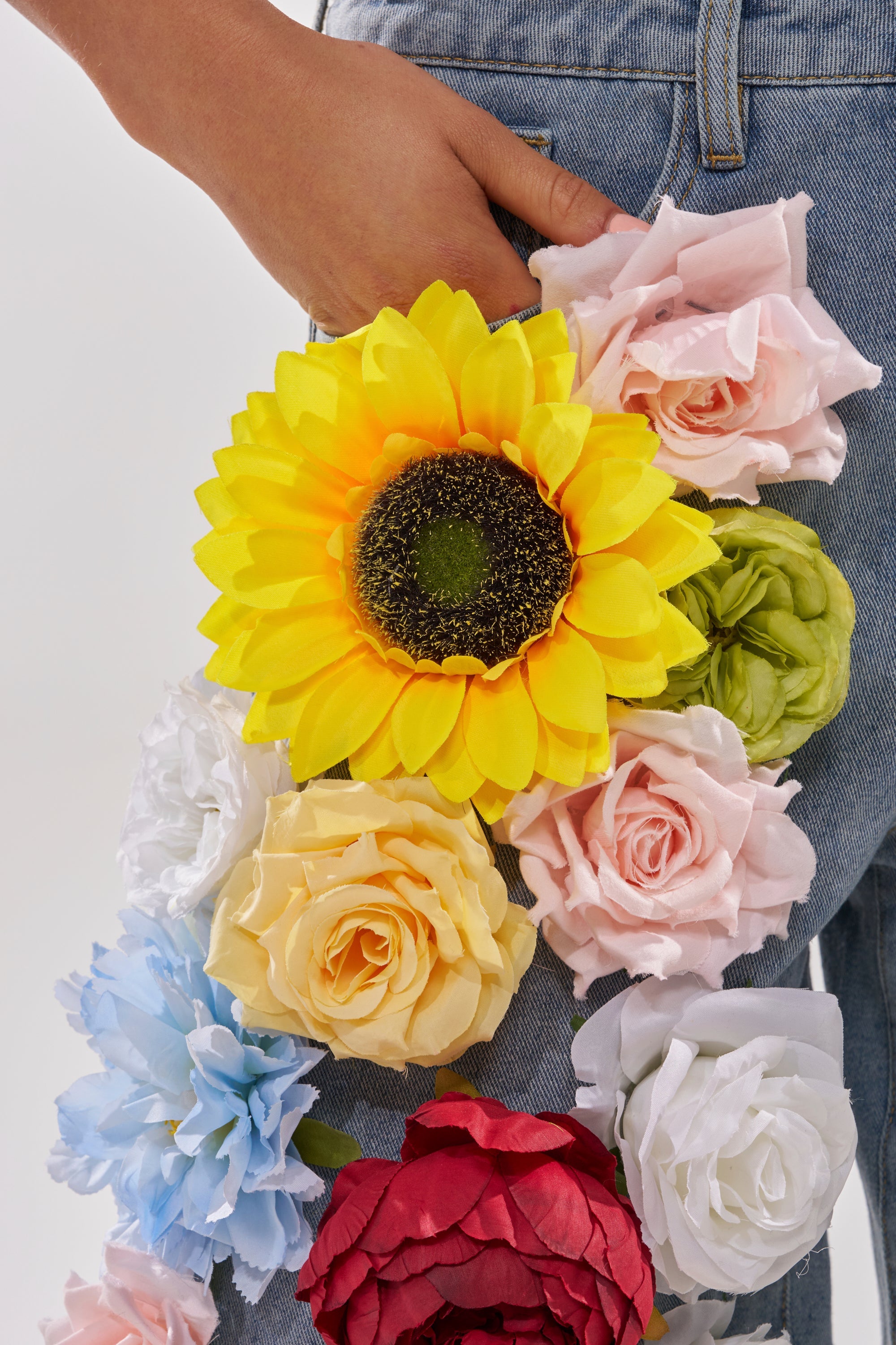 Wearing the FLOWER POWER BERMUDA SHORT, decorated with vibrant floral appliques like a big yellow sunflower and roses, a person stands with their hand in their pocket. 6