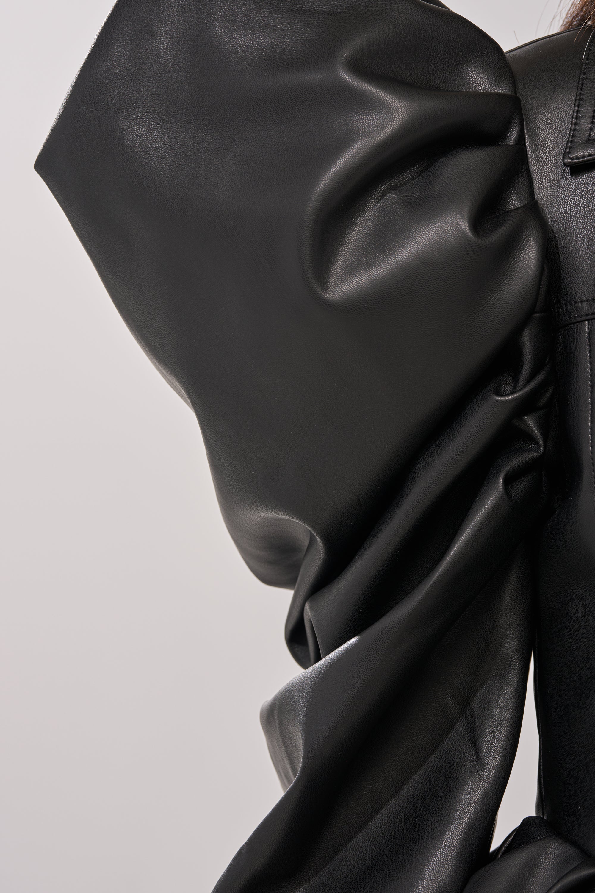 Close-up of the NIGHT MOVES FAUX LEATHER JACKET’s voluminous black sleeve featuring dramatic, sculptural folds and bold puff shoulders against a plain light background. 8