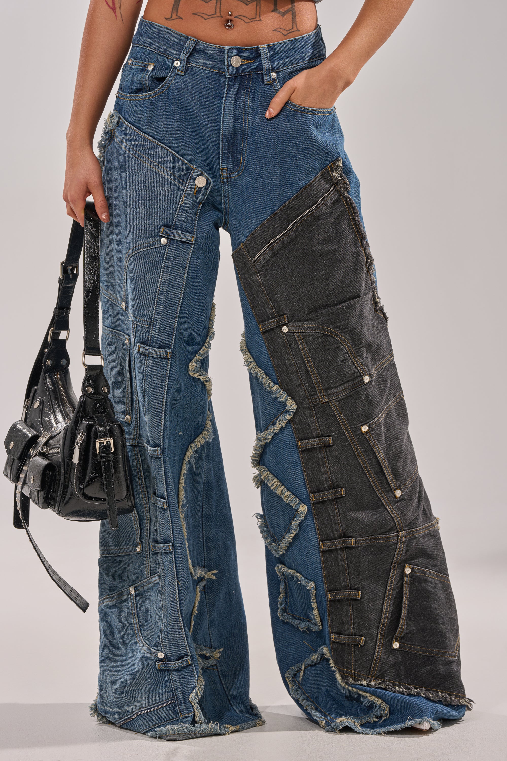 A person wears the MIXED MATCH RELAXED DENIM, wide-leg patchwork jeans with frayed seams, irregular denim shades, visible pockets, and metal rivets, styled with a black handbag. 2