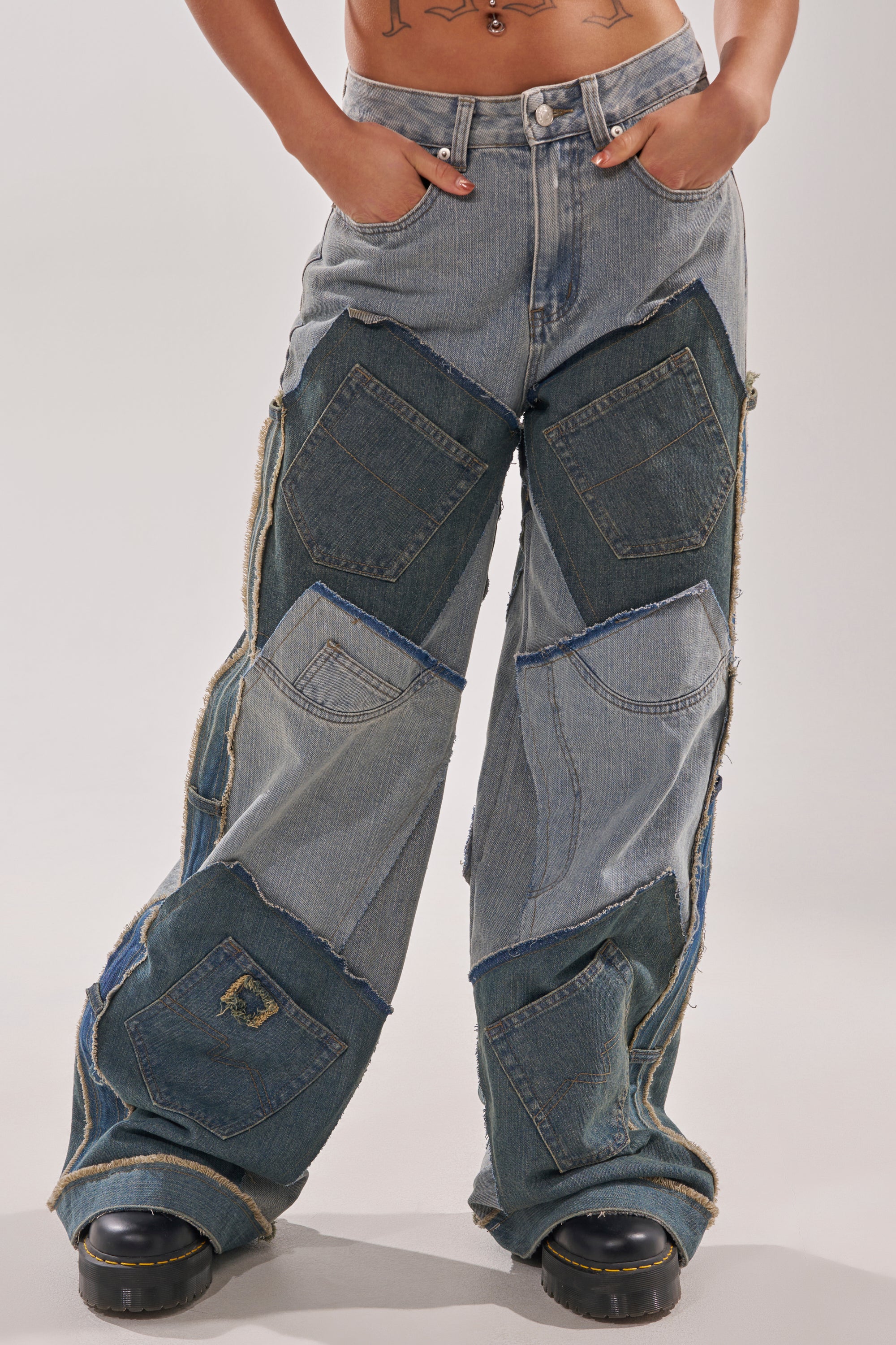 Channeling Y2K street style, they wear ALL THAT WIDE LEG DENIM JEANS—distressed patchwork, raw edges, visible pockets—with hands tucked in and midriff exposed, finished with bold black platform shoes. 0