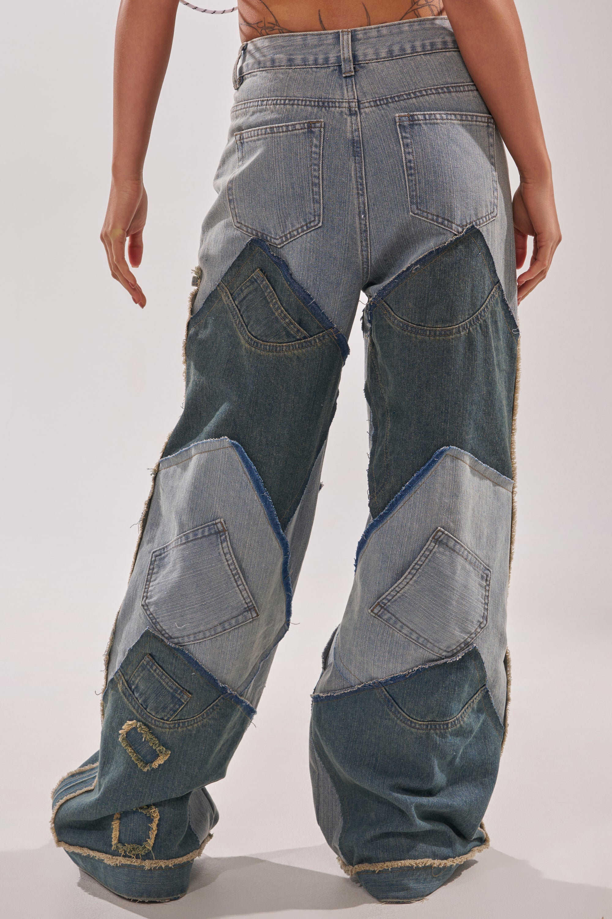Someone stands against a plain background wearing ALL THAT WIDE LEG DENIM JEANS, styled in true Y2K fashion with loose fit, patchwork in various denim shades, visible pockets, and frayed seams on the back and legs. 3