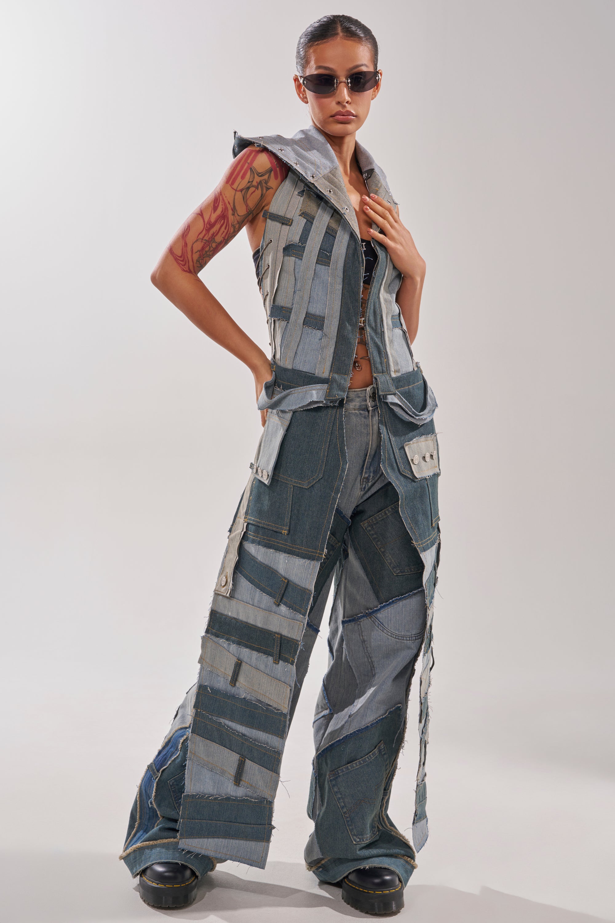 Wearing ALL THAT WIDE LEG DENIM JEANS, a person poses confidently in Y2K style with blue and gray patchwork, paired with sunglasses, a sleeveless hooded vest, and bold black platform shoes. 6