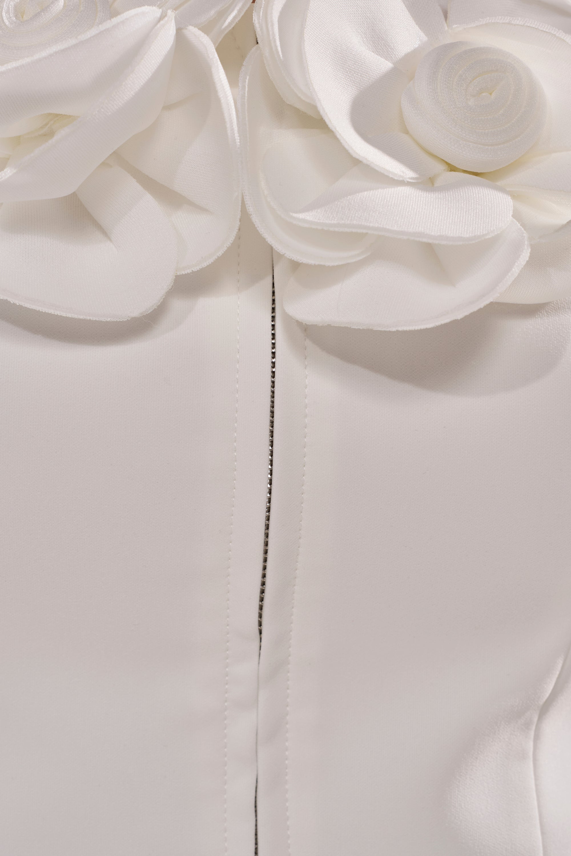 Close-up of the BRING ME FLOWERS BLOUSE showing white fabric with a centered seam and a decorative 3D rosette appliqué at the top, featuring layered petal-like details—perfect for a romantic look. 9