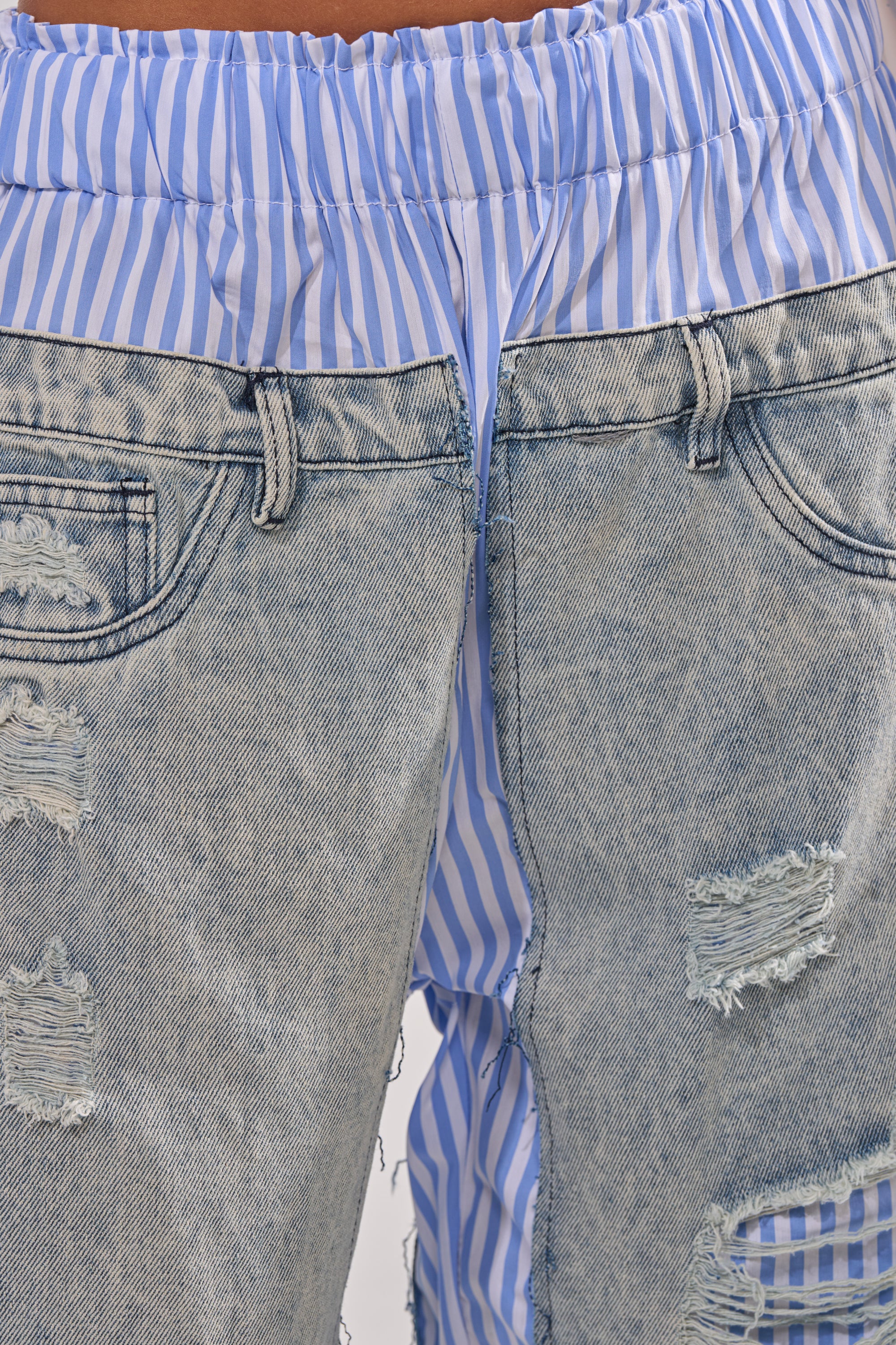Close-up of a person wearing the CALL IT WHAT YOU WANT MIXED UP TROUSER layered over blue-and-white vertical striped shorts, with the striped waistband peeking above for a bold street style statement. 8