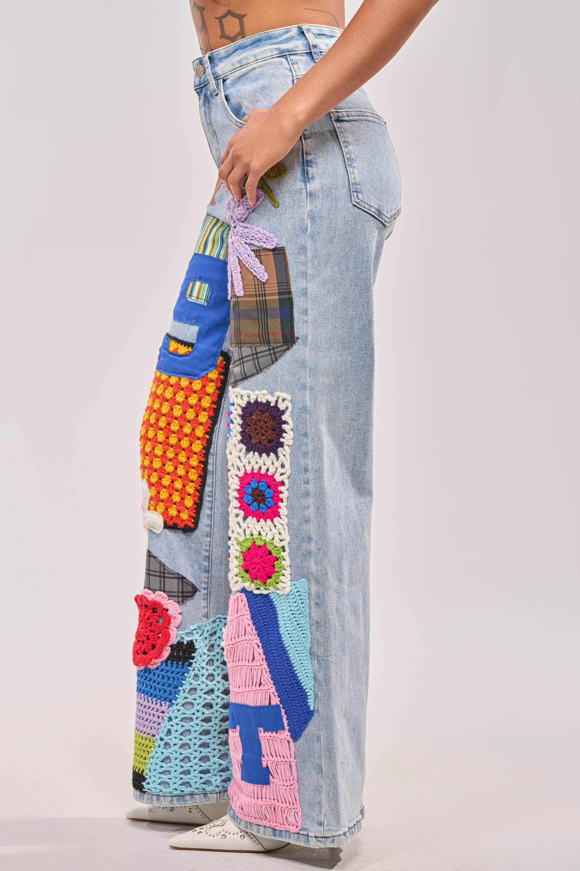 A person models the CUTE LIKE ME RELAXED DENIM—light-wash, wide-leg jeans with crochet patchwork—against a plain backdrop, showing only the lower torso and legs for a trendy street style look. 1