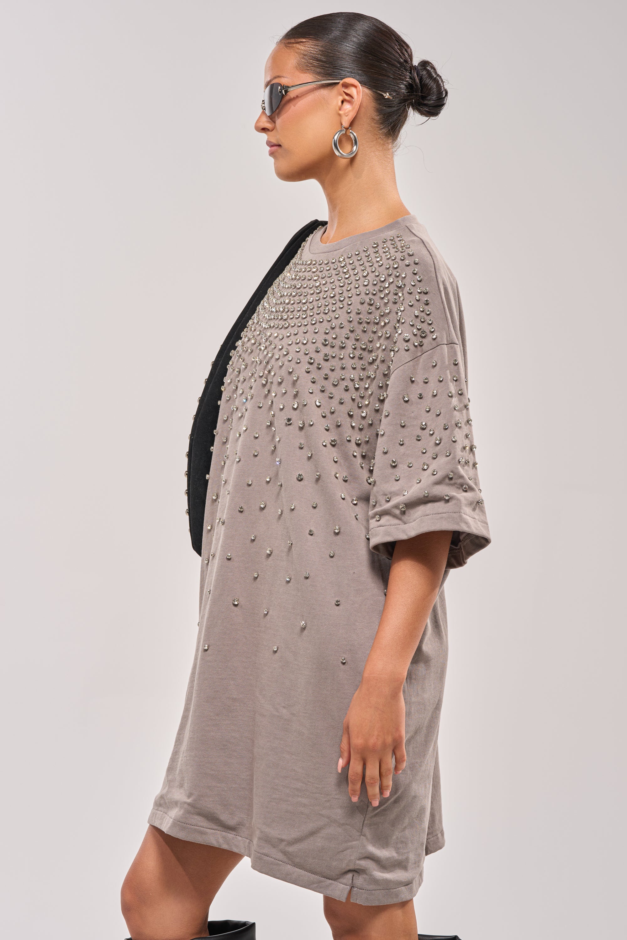 A woman in the IN MY ELEMENT RHINESTONE TEE SHIRT MINI DRESS, sunglasses, hoop earrings, and a black shoulder bag stands in profile against a plain light background. 4