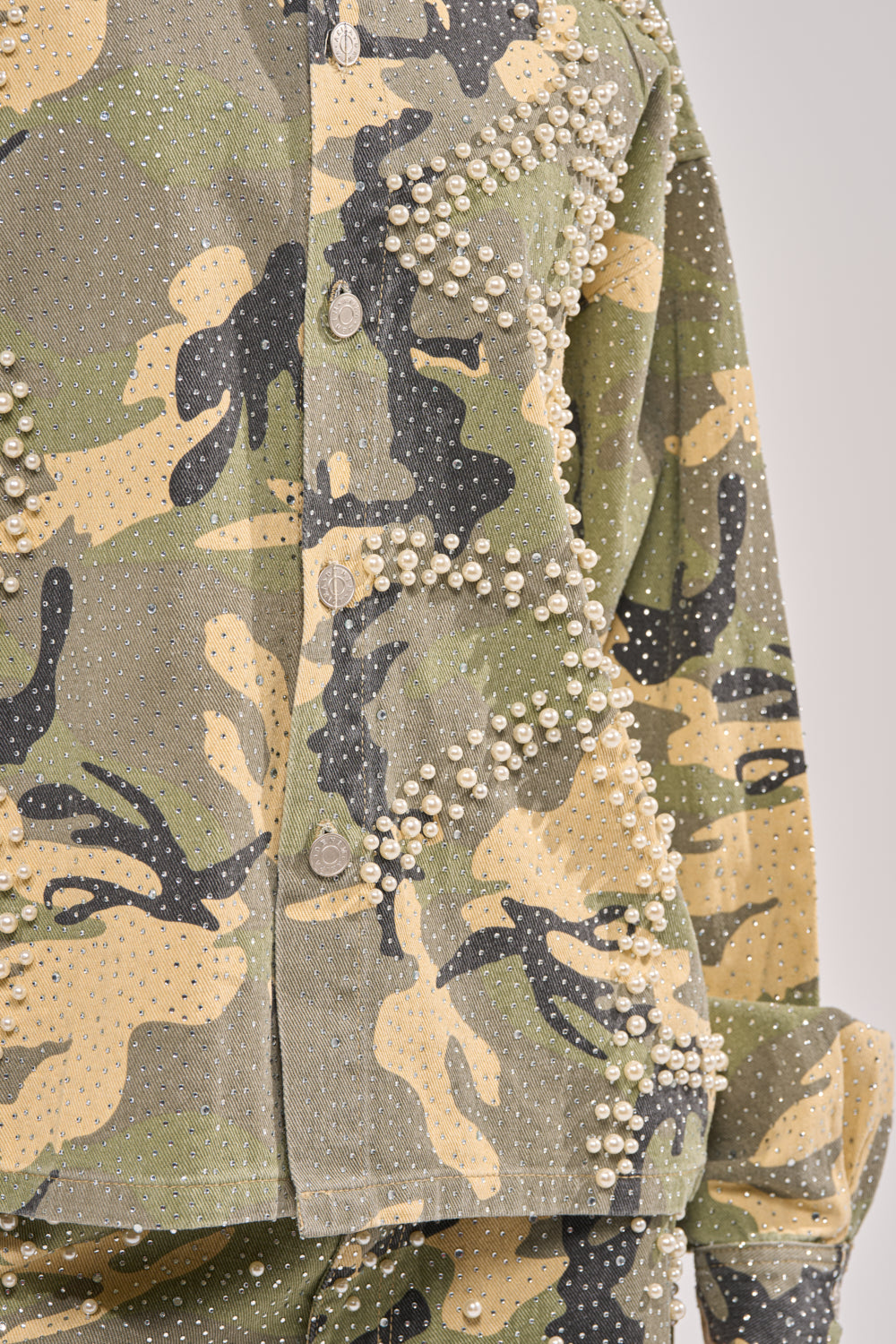 Close-up of the EMBELLISHED CAMO BUTTON DOWN, featuring pearls and rhinestones on green, beige, and black camouflage. This fashion button-down includes front buttons and matching camo sleeves. 9