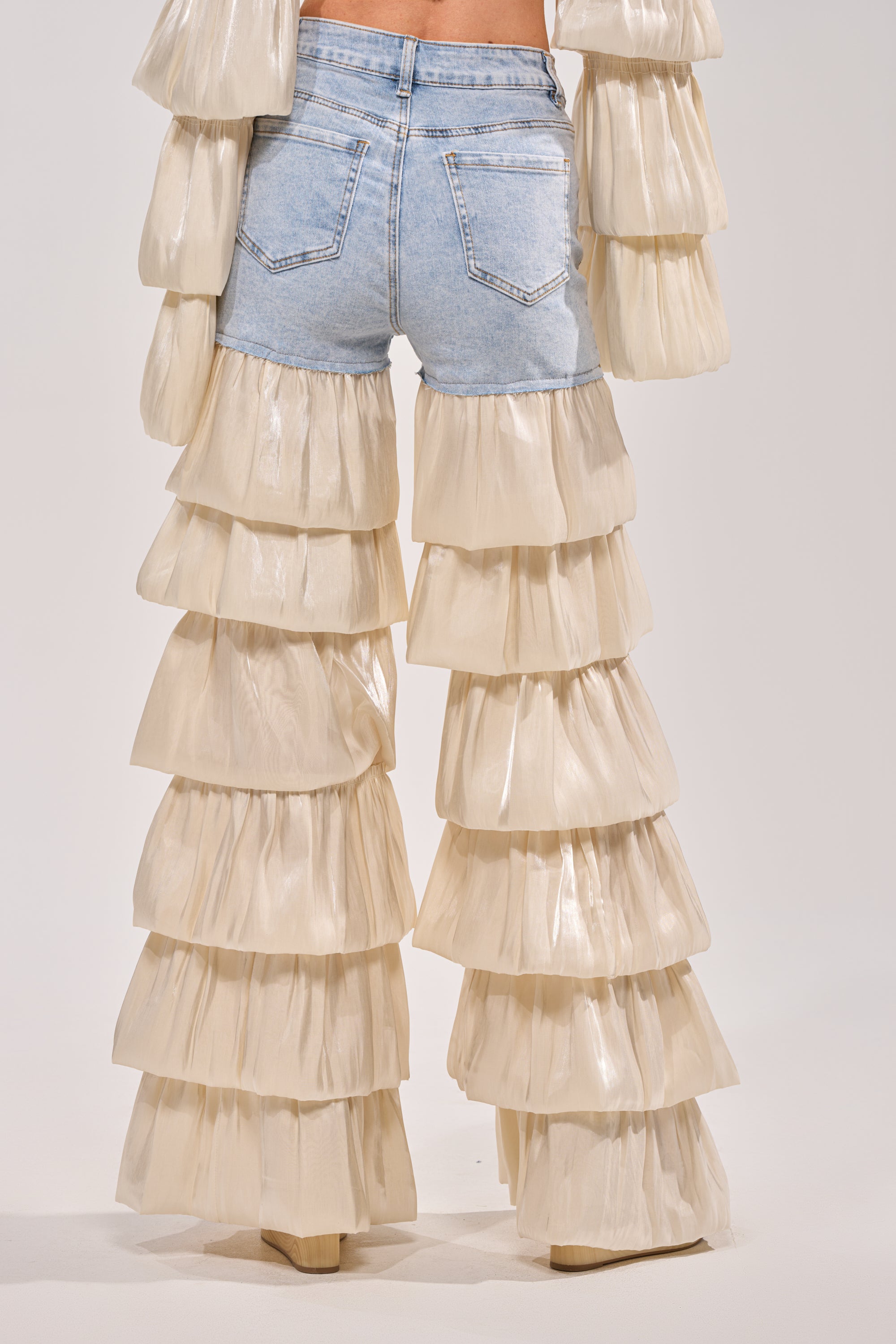 Wearing the BOUNCIN AROUND DENIM RUFFLE PANT in light blue, this look features dramatic bell-bottom legs with tiered cream organza ruffle layers for a bold, party-ready statement. 3