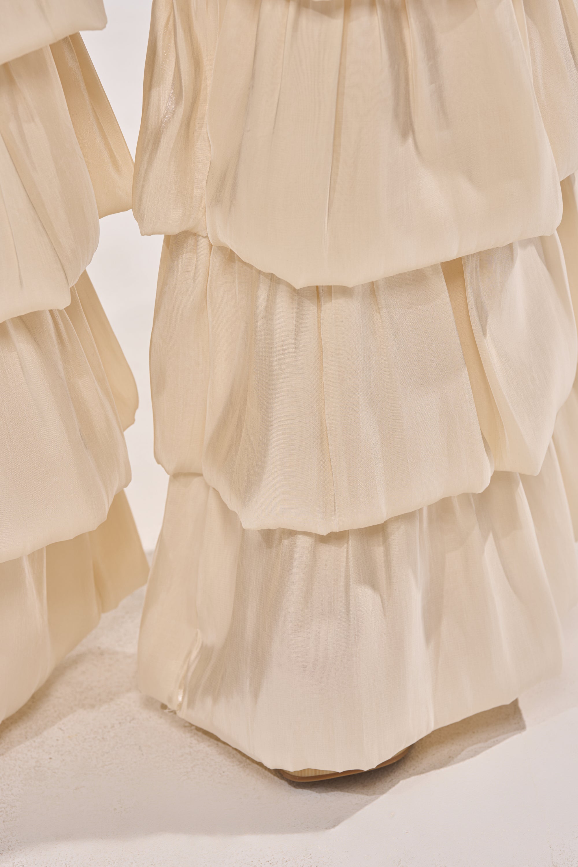 Close-up of cream-colored organza ruffles on the BOUNCIN AROUND DENIM RUFFLE PANT, featuring soft, tiered layers cascading vertically. The neutral background and light surface highlight the playful party-ready design. 6