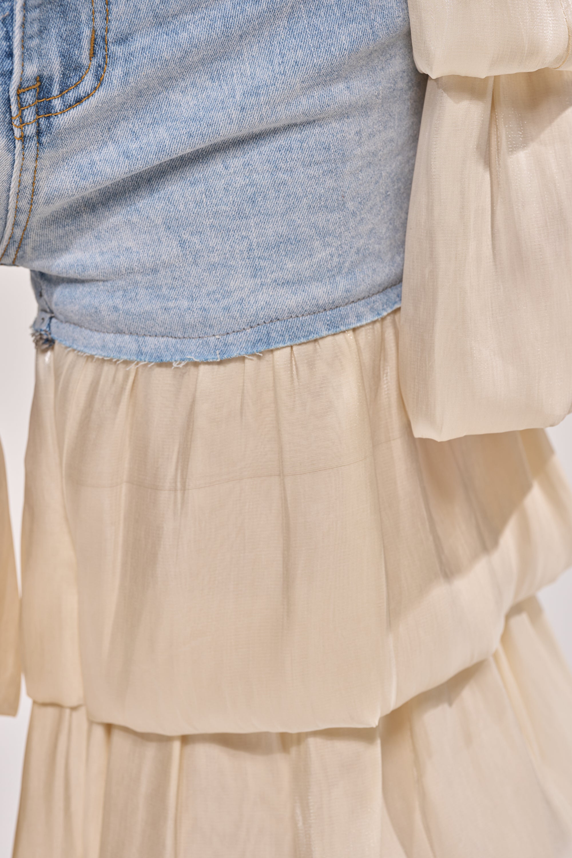 Close-up of the BOUNCIN AROUND DENIM RUFFLE PANT, featuring light-wash denim shorts under a sheer, layered cream skirt with matching tiered organza ruffle sleeves, blending casual and elegant fashion elements. 7