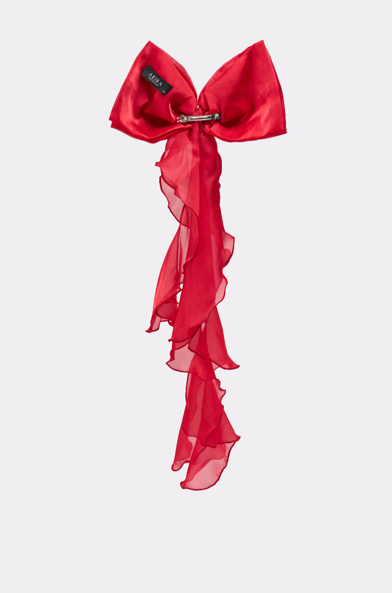 The HEY DOLL CHIFFON HAIR BOW features an oversized, sheer red bow with flowing ruffled ribbons and a black label by the knot, making a striking hair accessory displayed against a plain light background. 4