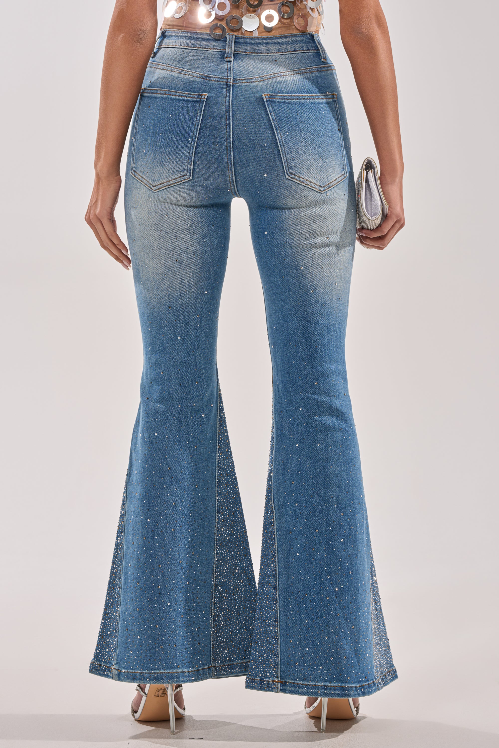 A person is seen from the back wearing BLING BLING FLARE DENIM with sparkling rhinestone embellishments, styled with tan high heels and a small silver clutch. 4