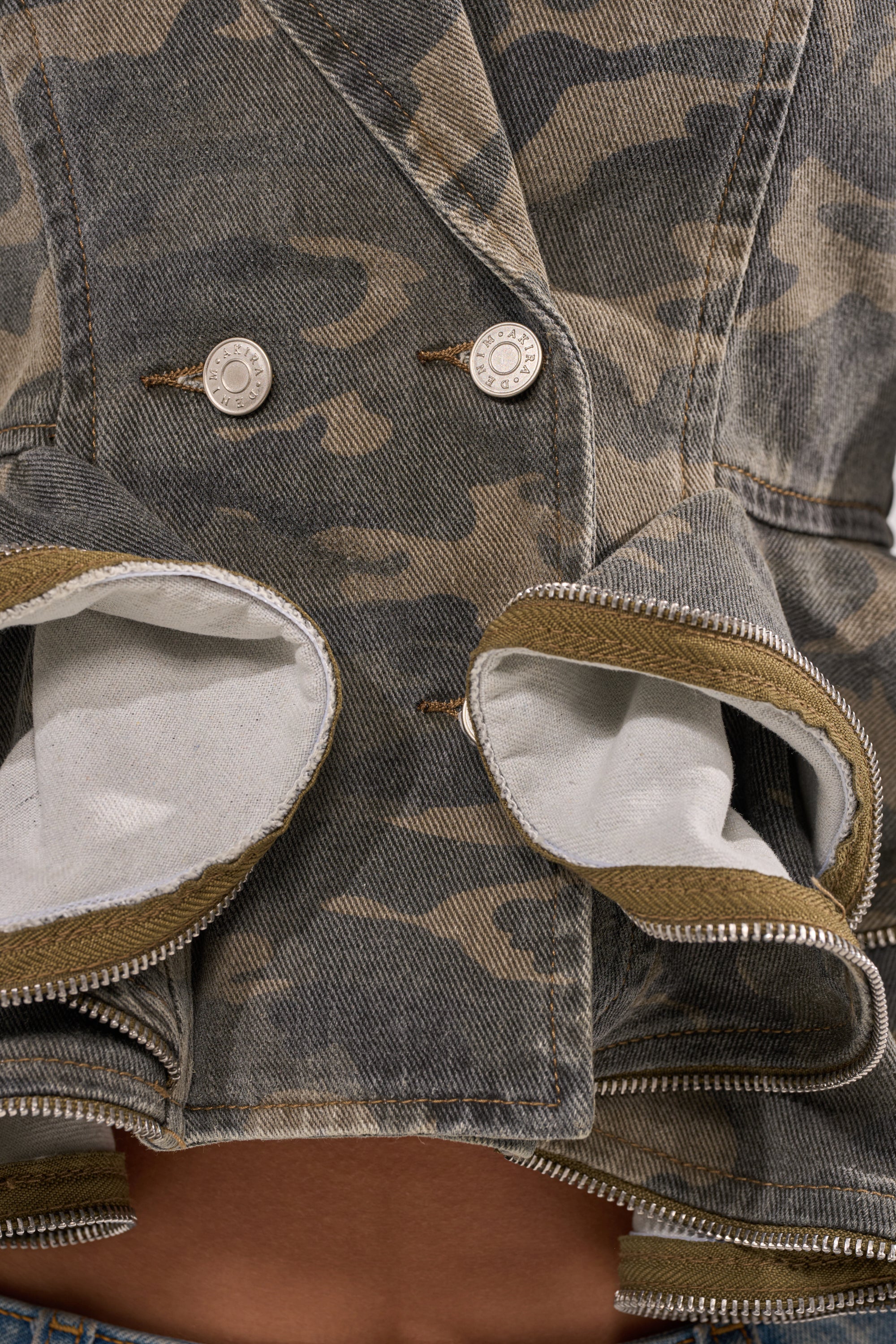 Close-up of the PEPLUM CAMO JACKET featuring silver buttons and bold front zippers, highlighting its street style construction and contrasting inner fabric. 7