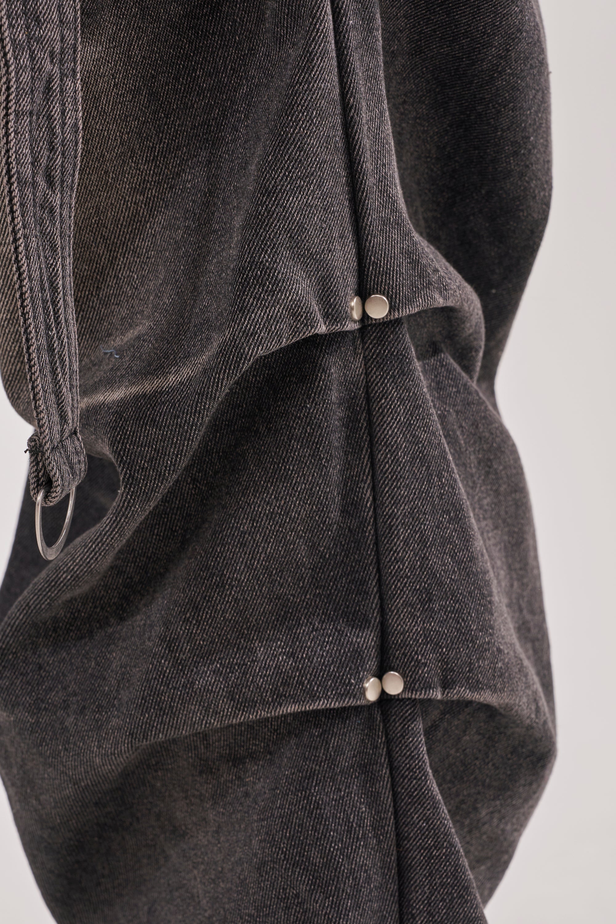 Close-up of LEGEND TROUSER: black wide-leg cargo denim pants featuring two silver snap buttons securing overlapping folds for a structured, layered look inspired by western streetwear. 11