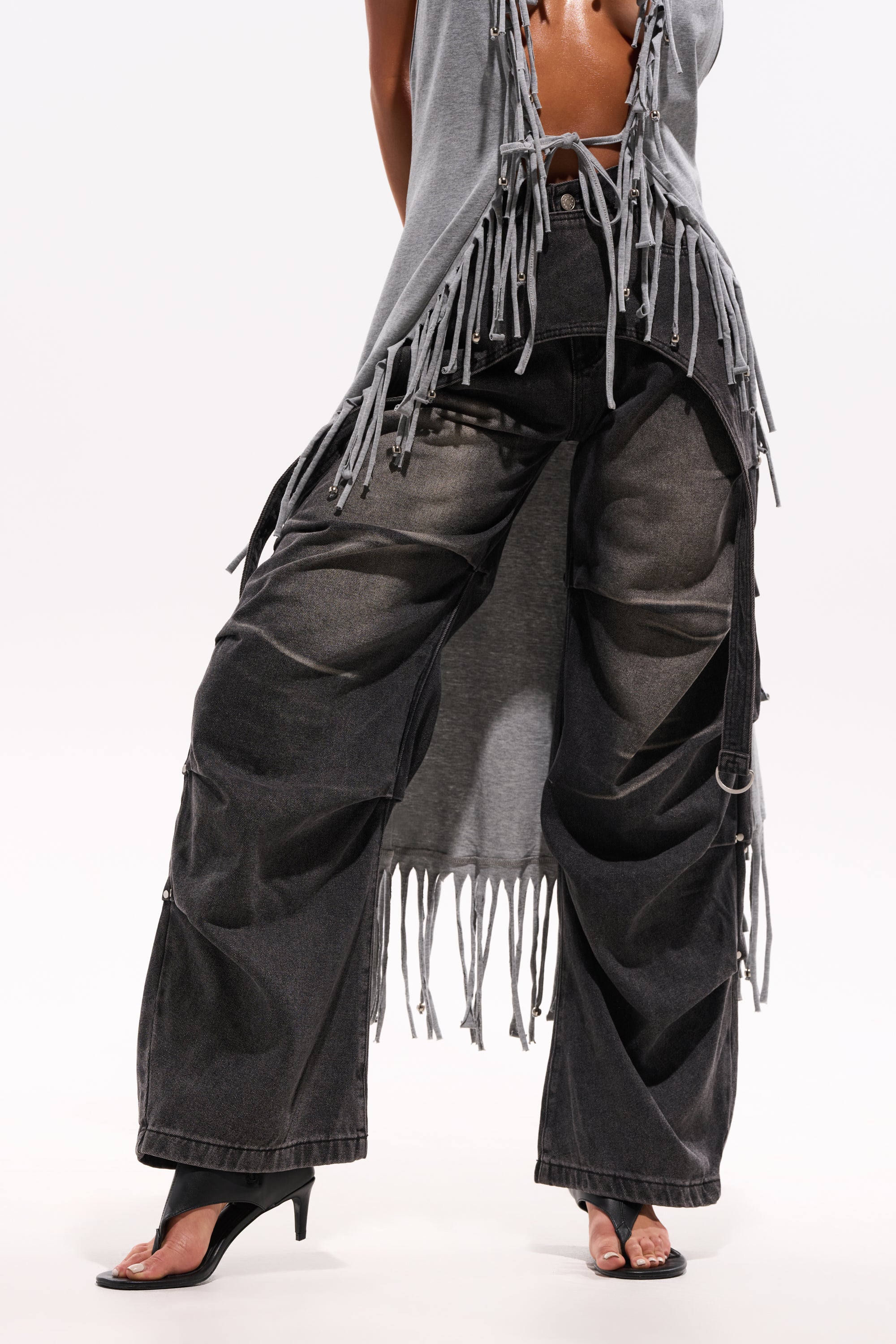 A person in LEGEND TROUSER black wide-leg cargo denim pants, black open-toe heels, and a sleeveless gray top with fringe, standing against a plain white background. 0