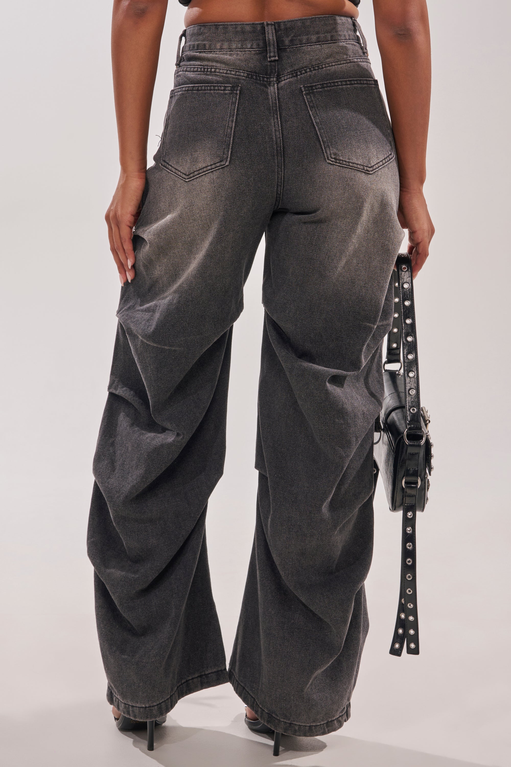 A person is seen from the back wearing LEGEND TROUSER high-waisted black wide-leg cargo denim pants with black heels and a black studded handbag, capturing a western streetwear vibe. 7