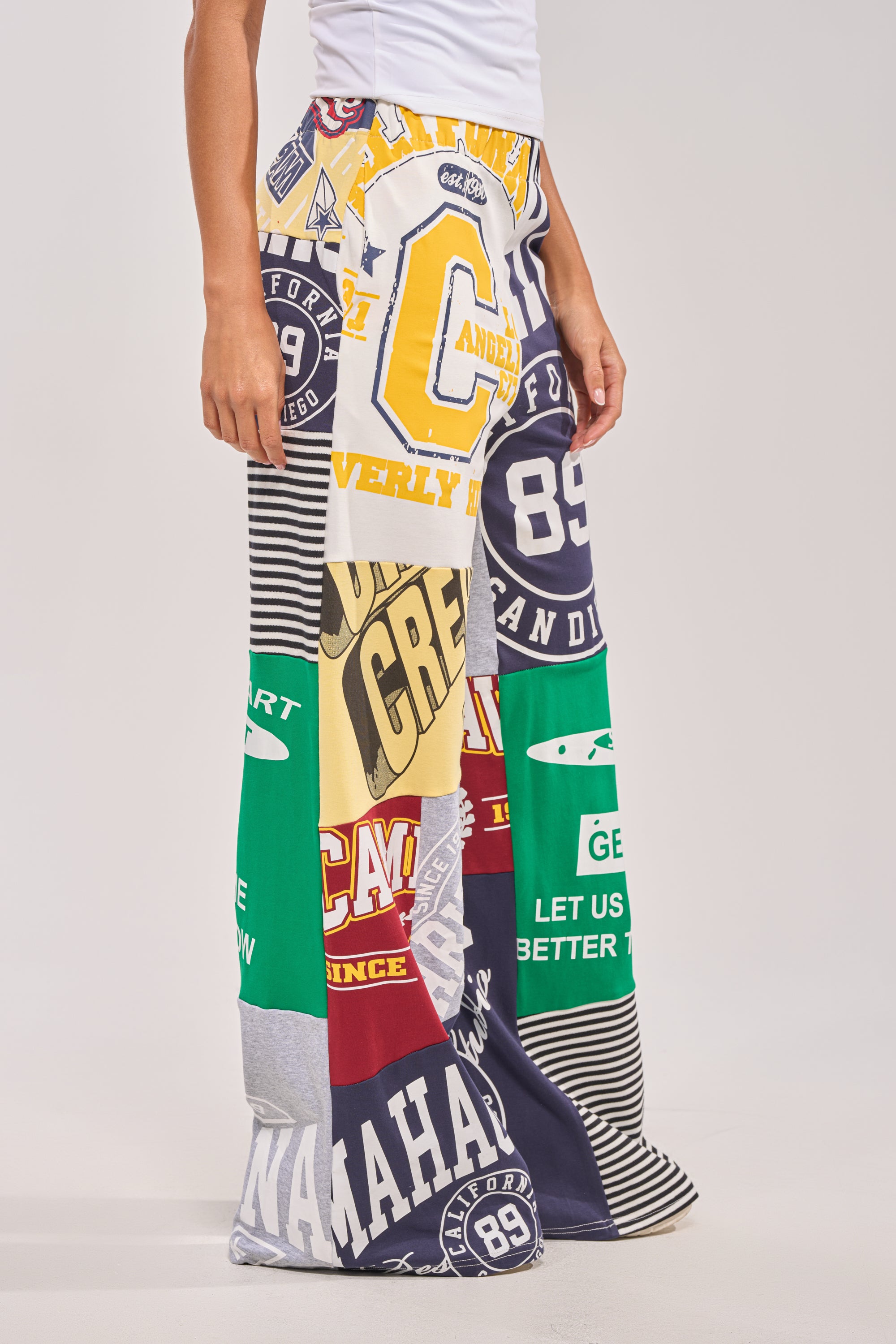 Someone wearing the GAME TIME PATCHWORK JOGGER—wide-leg joggers made from colorful, graphic T-shirts and sweatshirts, featuring bold letters, numbers, and logos in a standout streetwear-inspired design. 4