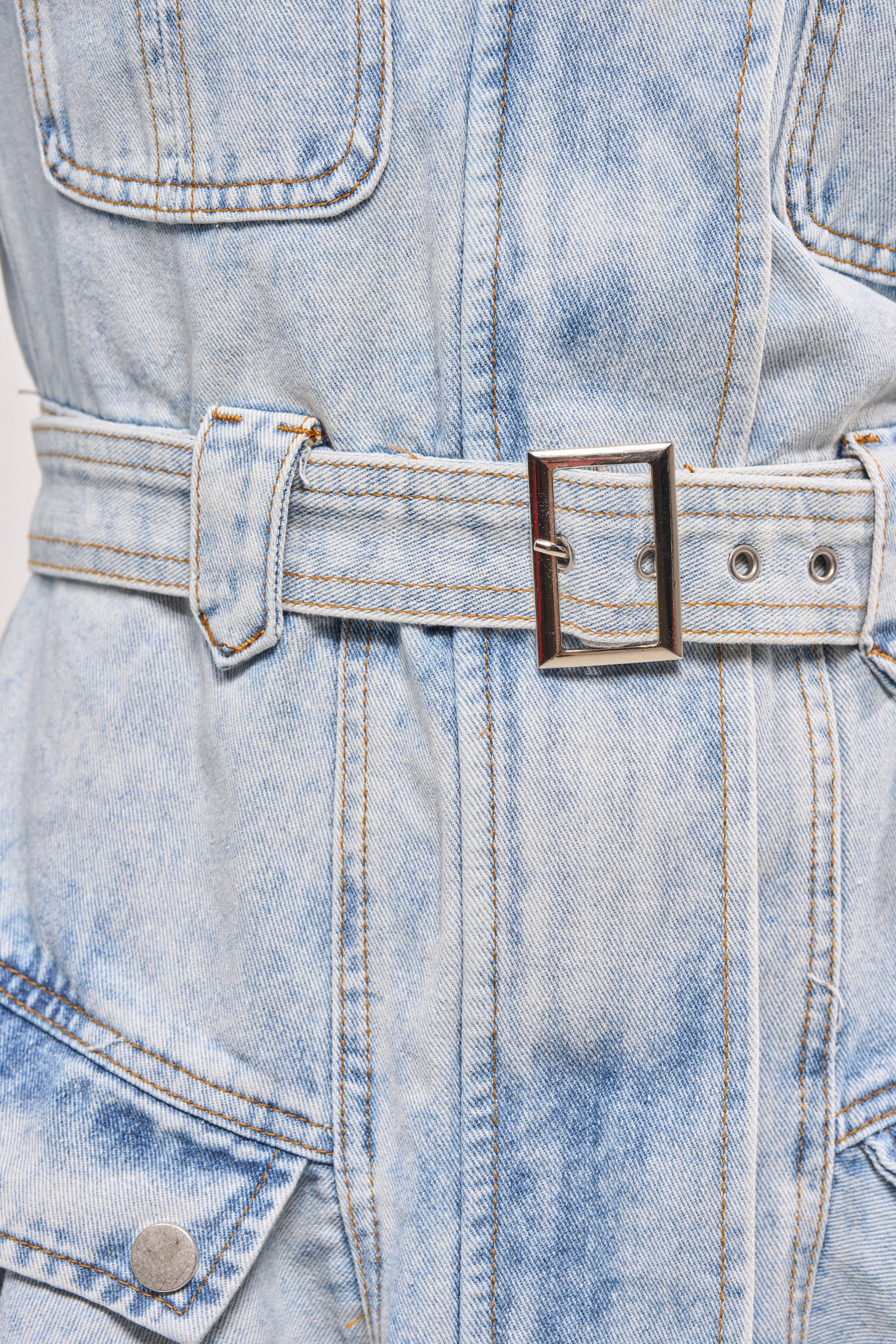 Close-up of the SAY PRETTY PLEASE DENIM MINI DRESS in light blue acid-wash, showcasing a belted waist with metal buckle, visible stitching, and pockets accented by silver buttons. 7