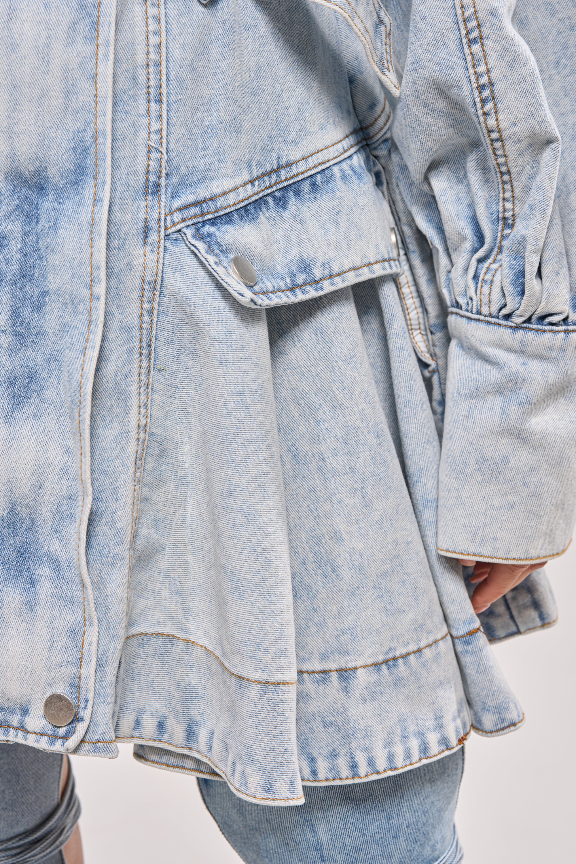 A close-up of the SAY PRETTY PLEASE DENIM MINI DRESS in light blue acid-wash, featuring metal buttons, a flap pocket, gathered sleeves, and a matching belt. 8