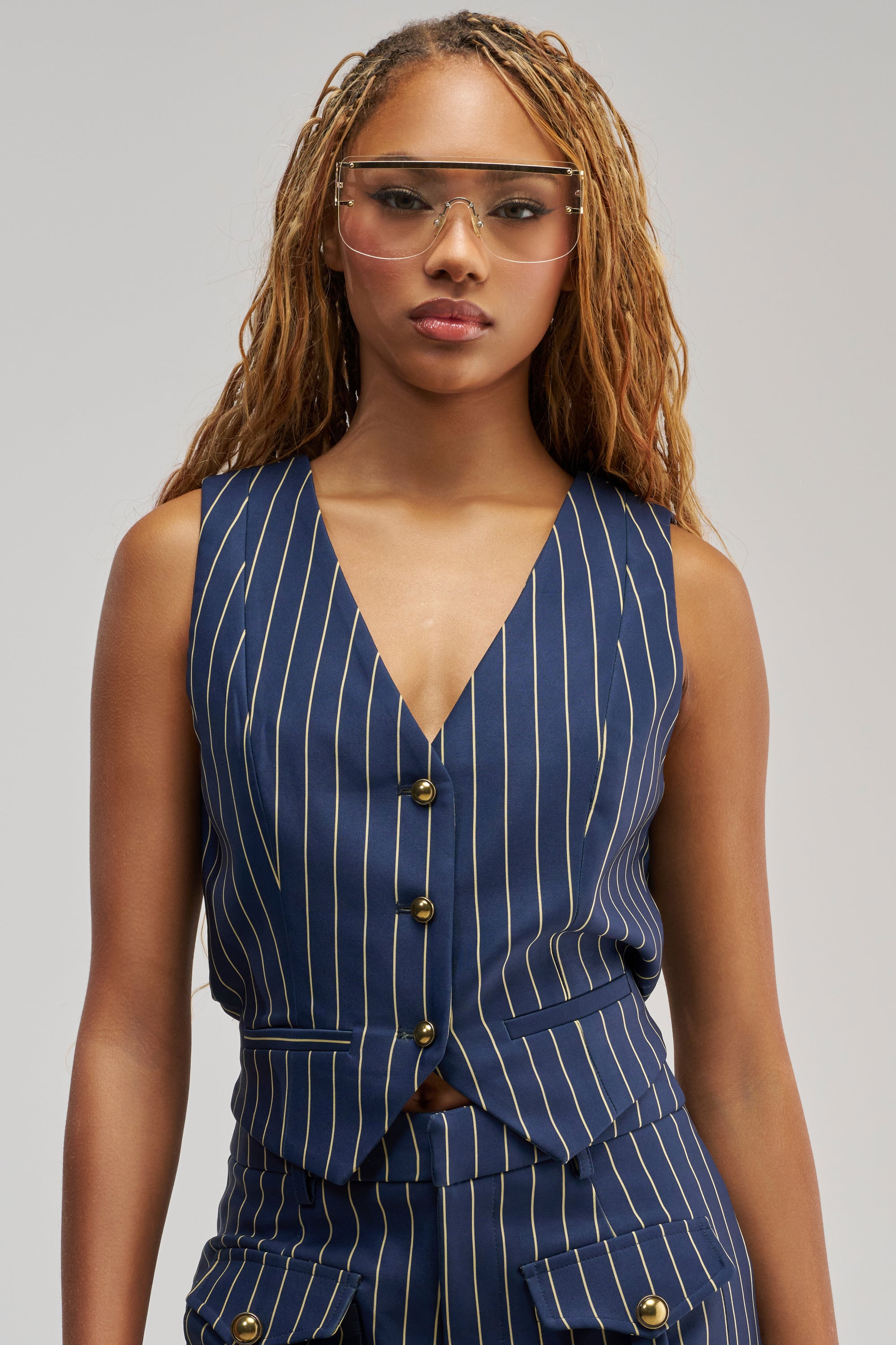 Wearing the SUNDAY PINSTRIPE VEST as part of a stylish three-piece suit, a person with long, light brown braided hair and clear glasses stands against a plain gray background.