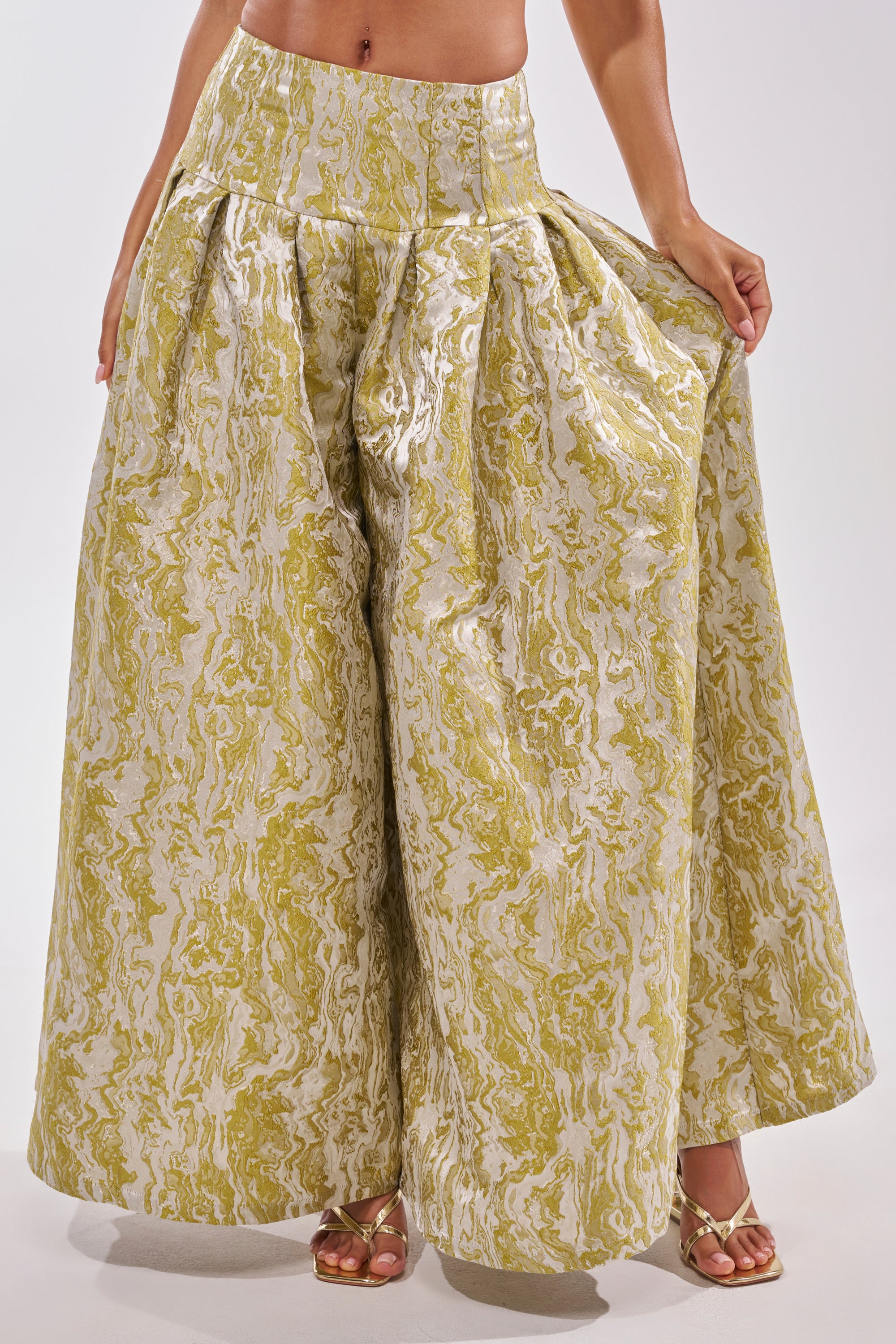 A person models the GET IT FLORAL TROUSER—wide-legged, high-waisted pants with a gold and white marble pattern—fanning out the sides for a statement brunch look. Gold sandals complete this standout outfit. 2