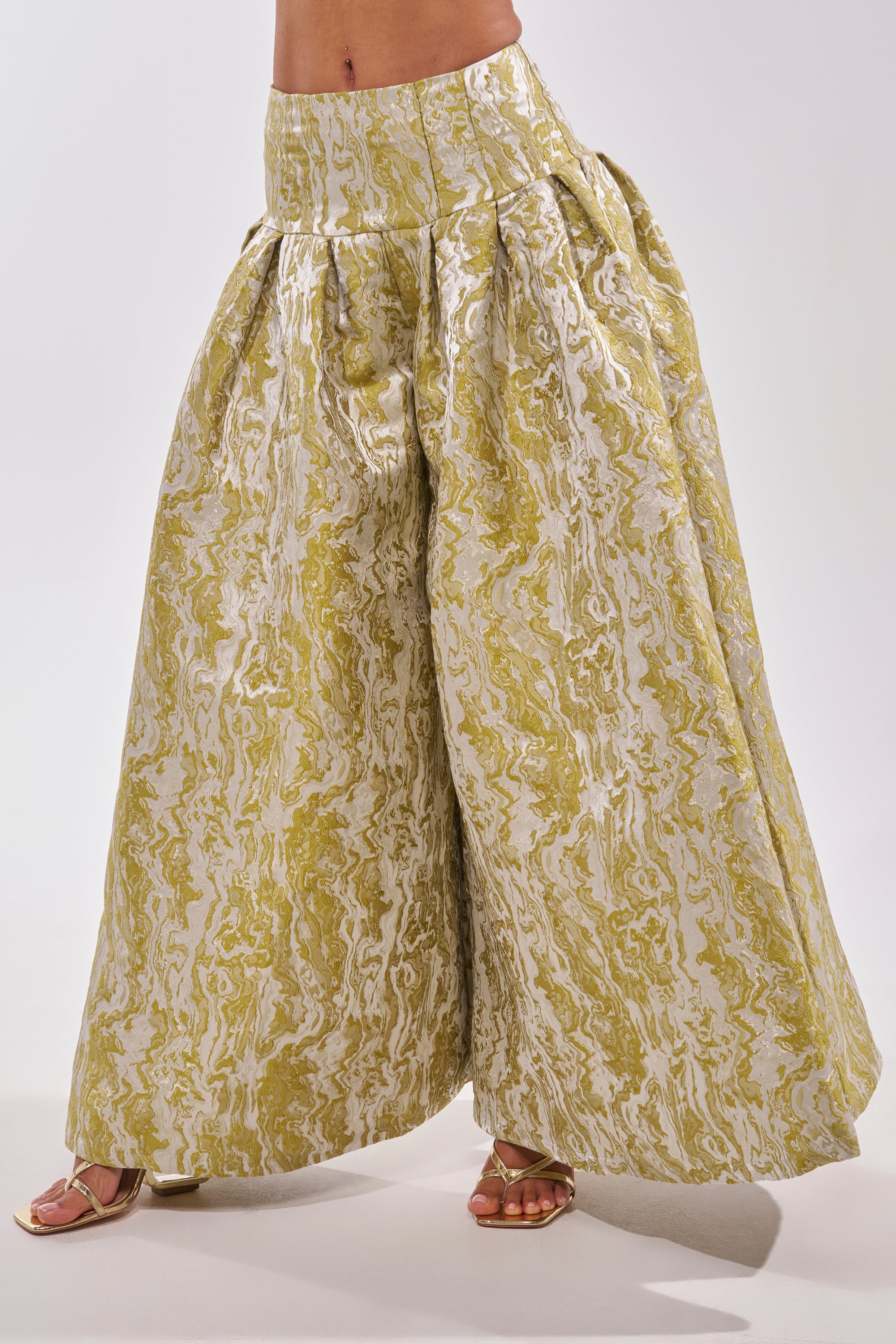 A person showcases statement brunch style in GET IT FLORAL TROUSER—wide-legged, high-waisted yellow and white marbled pants—paired with gold sandals against a plain white background. 3