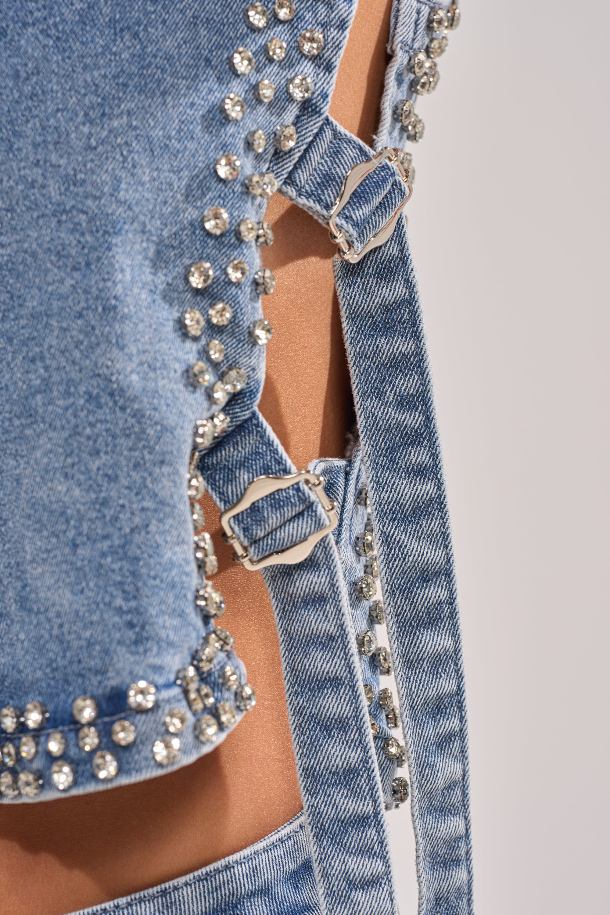 Close-up of the LOVE ME RHINESTONE DENIM TOP, featuring silver rhinestones, metal buckles, and side cutouts that reveal skin. The textured details and embellishments highlight this trendy festival-ready piece. 7