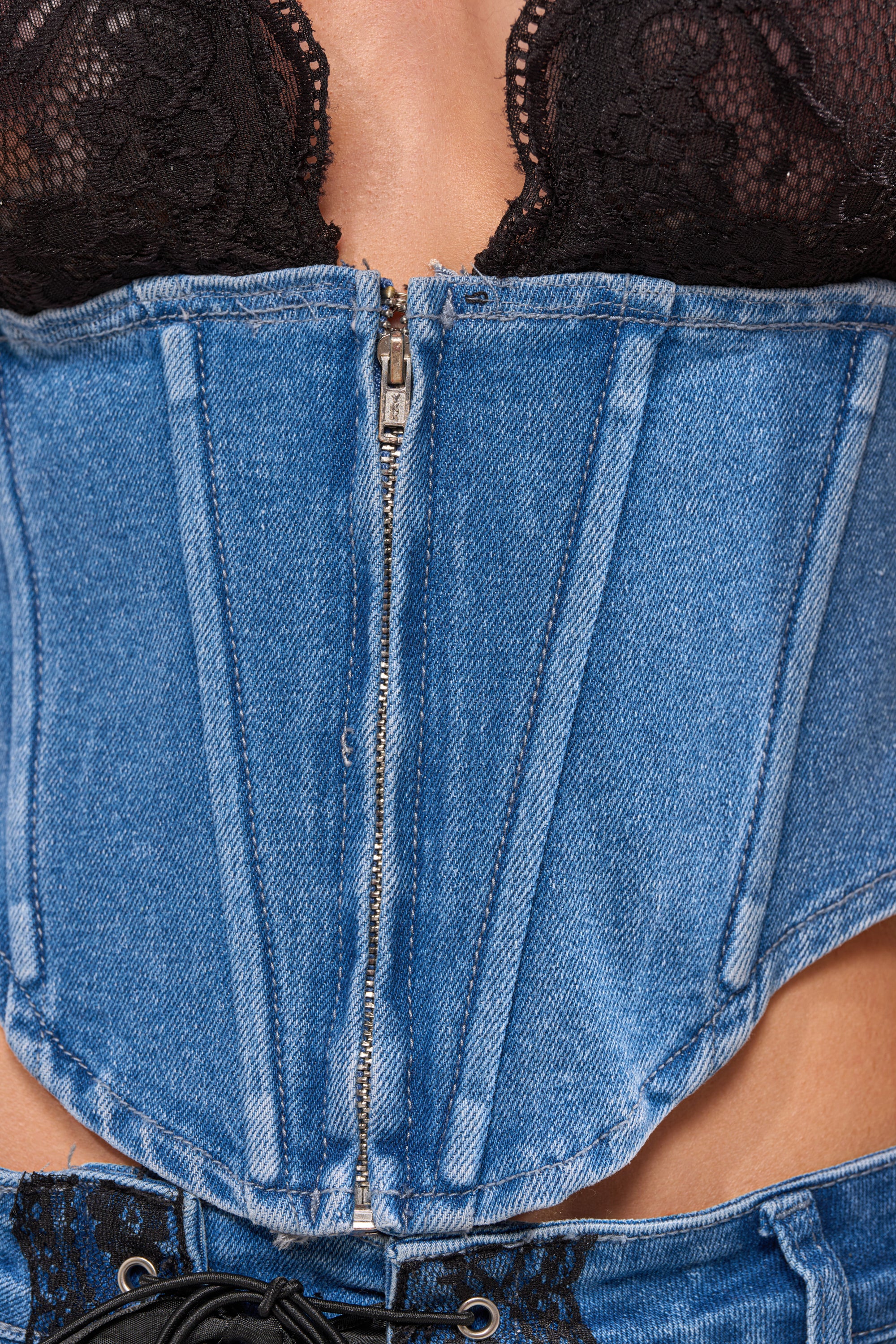 Close-up of a person wearing the LACED UP DENIM CORSET with a front zipper over a black lace bra, paired with matching blue denim bottoms visible at the bottom. 6