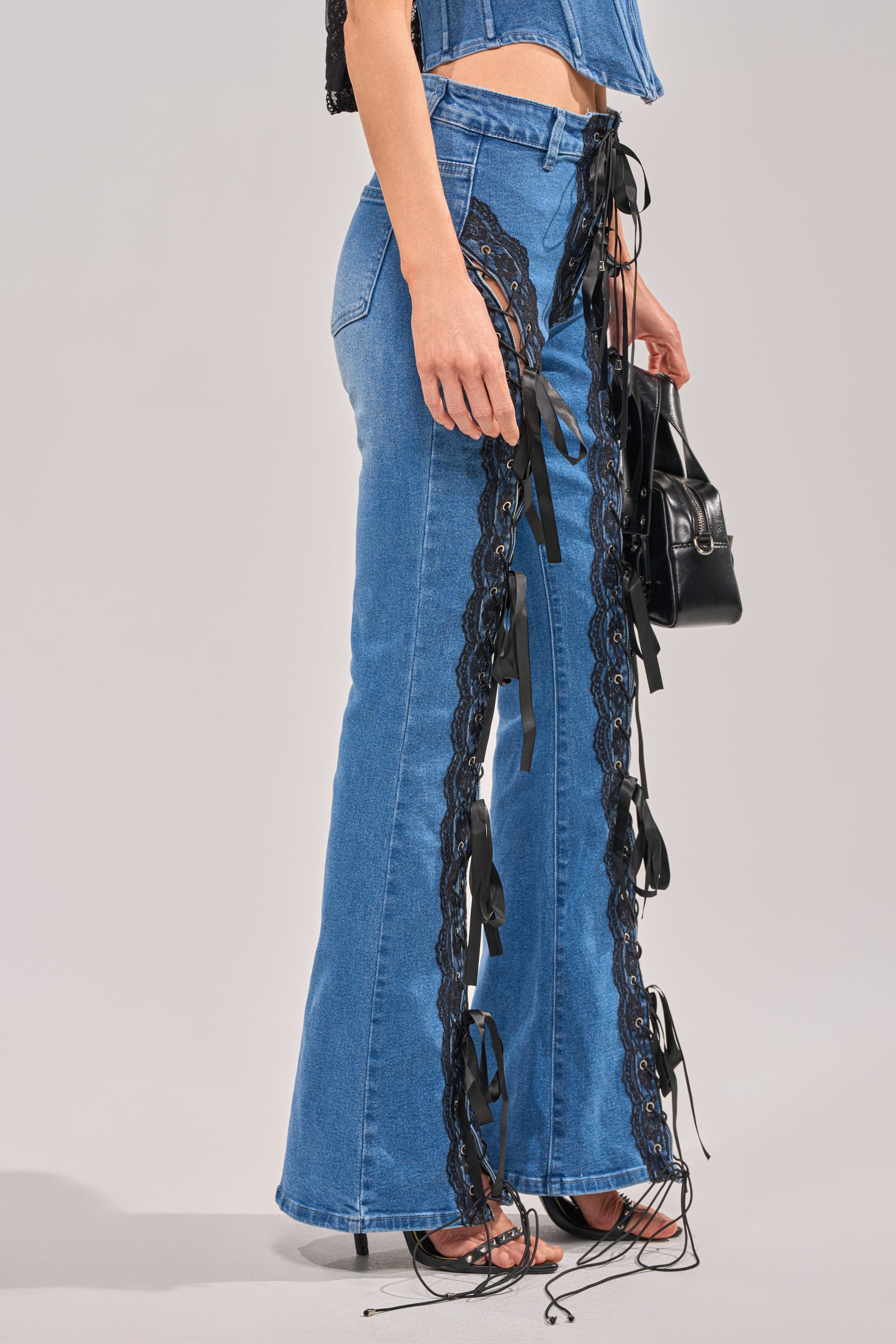 Wearing the LACED UP DENIM flared jeans with black lace trim and side ribbon details, styled with a denim top and small black handbag for a coordinated, chic look. 2