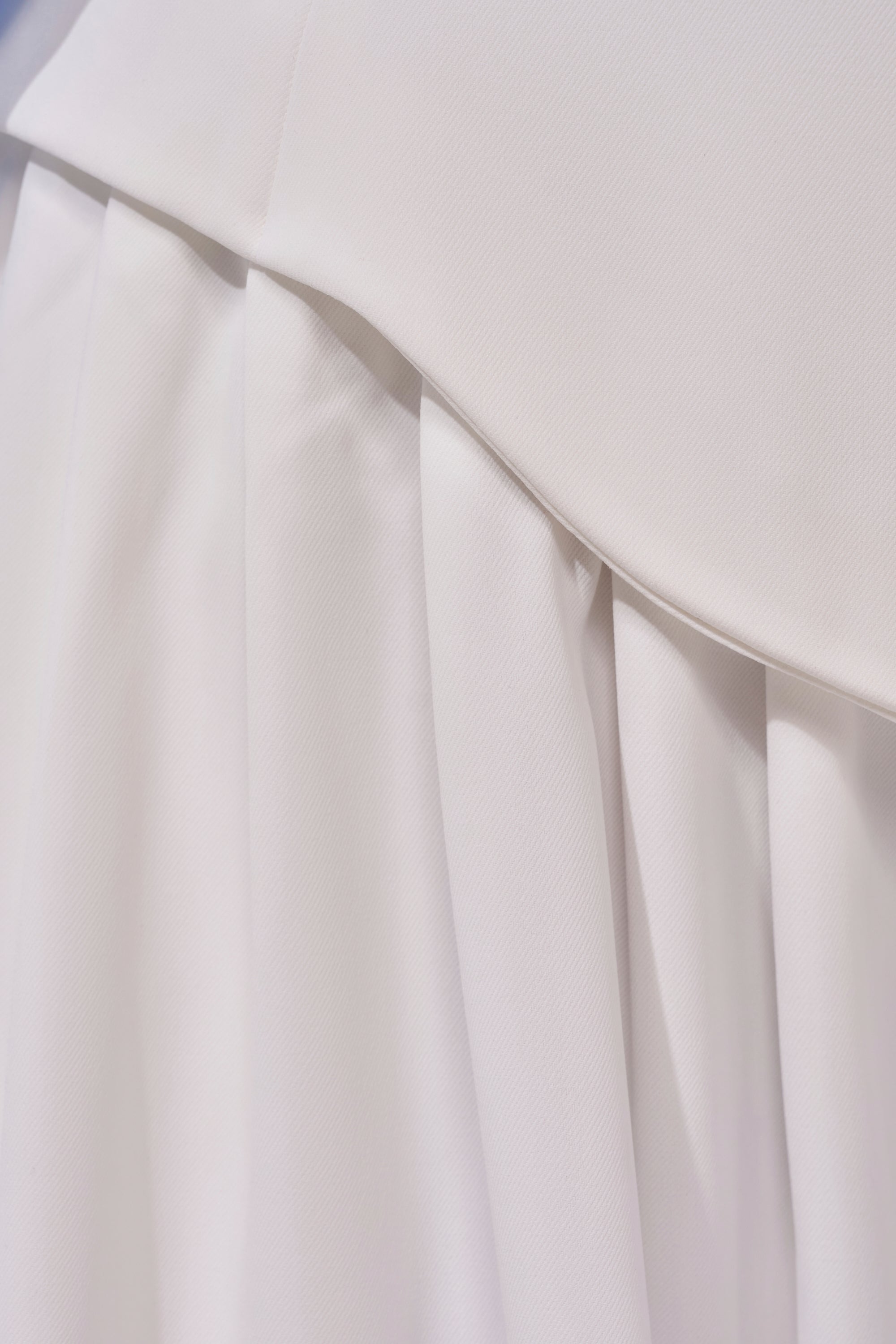 Close-up of the GALAXY TROUSER showcases white, pleated fabric with smooth texture and soft folds, emphasizing meticulous stitching and elegant craftsmanship. 8