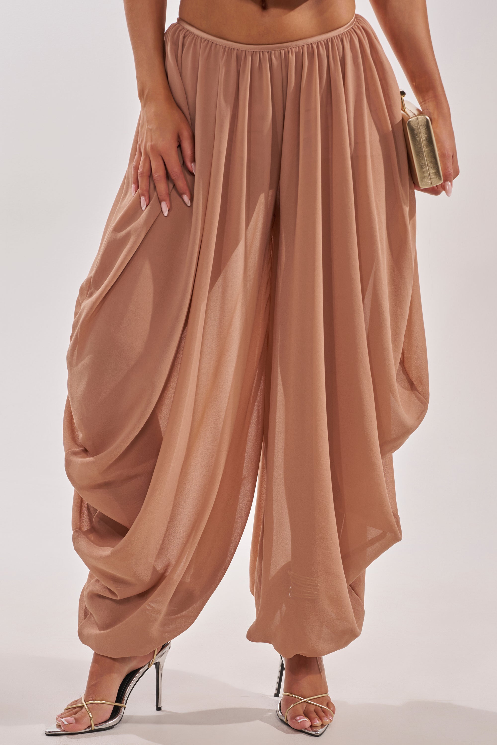 A person models the BOUNCIN AROUND BALLOON PANT in brown chiffon, paired with silver high-heeled sandals and a small metallic clutch, against a plain background. 1