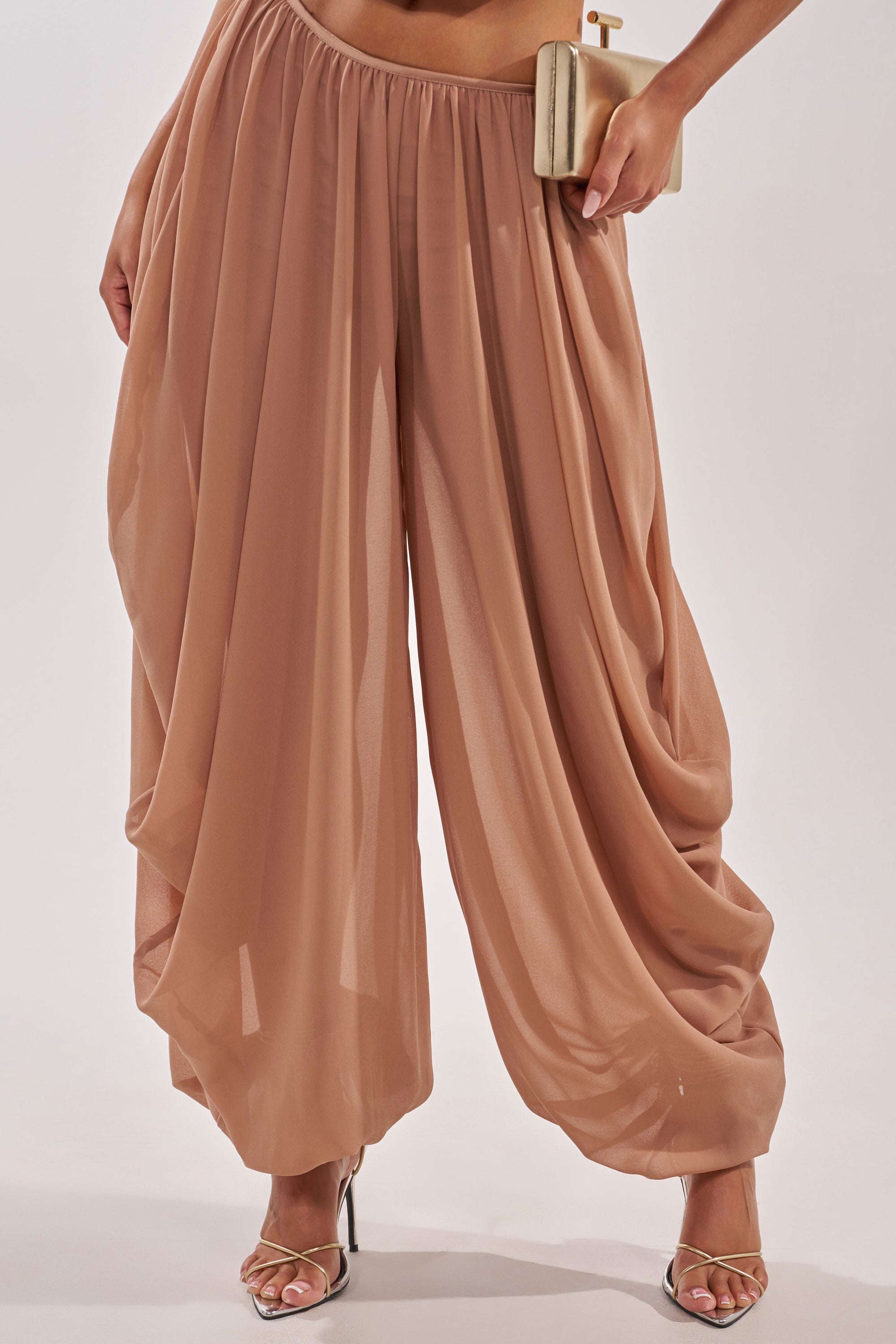 A person wears the BOUNCIN AROUND BALLOON PANT in taupe with an elastic waistband, paired with a beige clutch and silver high-heeled sandals. The image is cropped at the waist and ankles. 2