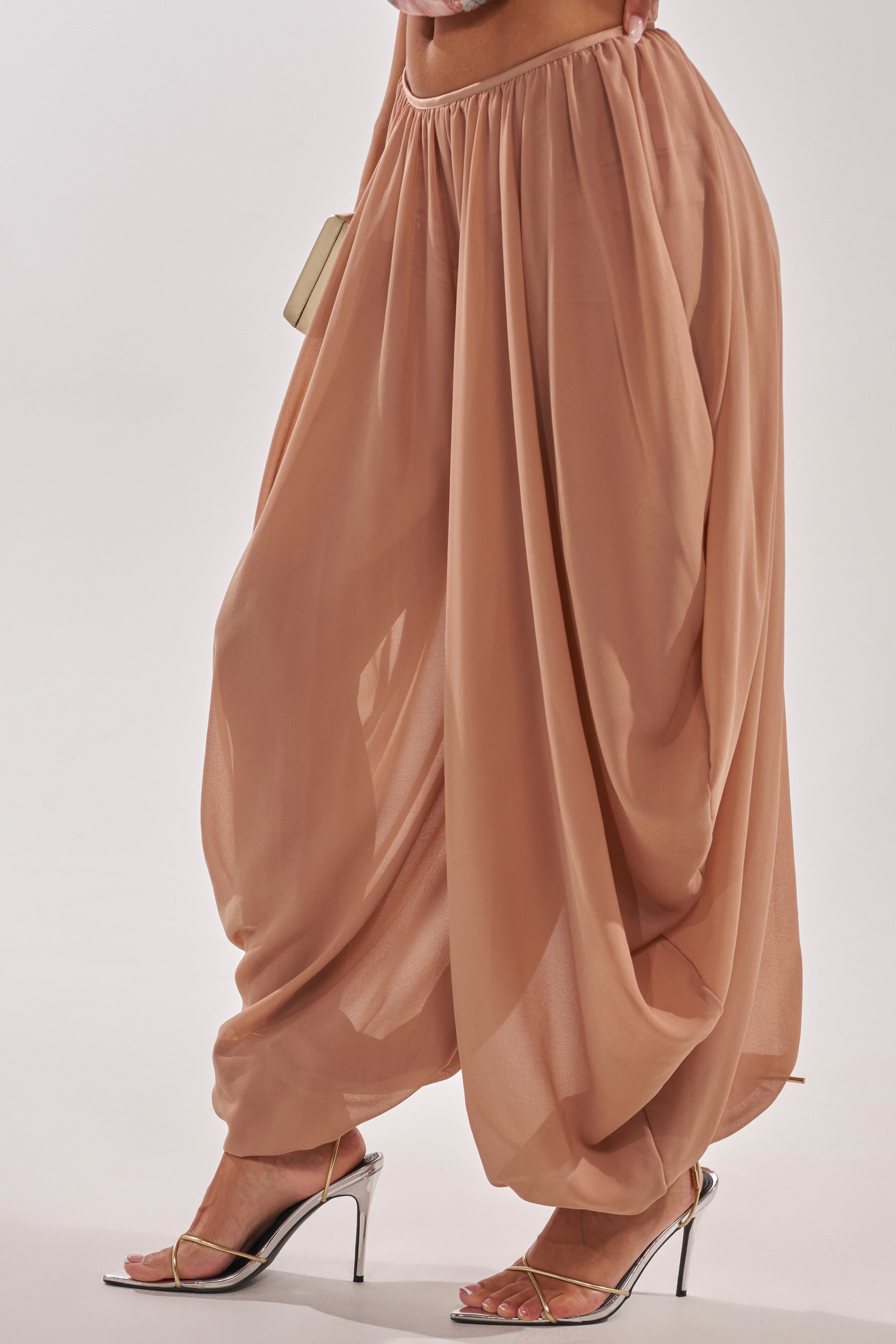 Wearing the BOUNCIN AROUND BALLOON PANT in peach with loose, draped wide legs and silver high-heeled sandals, holding a small beige clutch. The photo is cropped to show only the lower torso and legs. 3