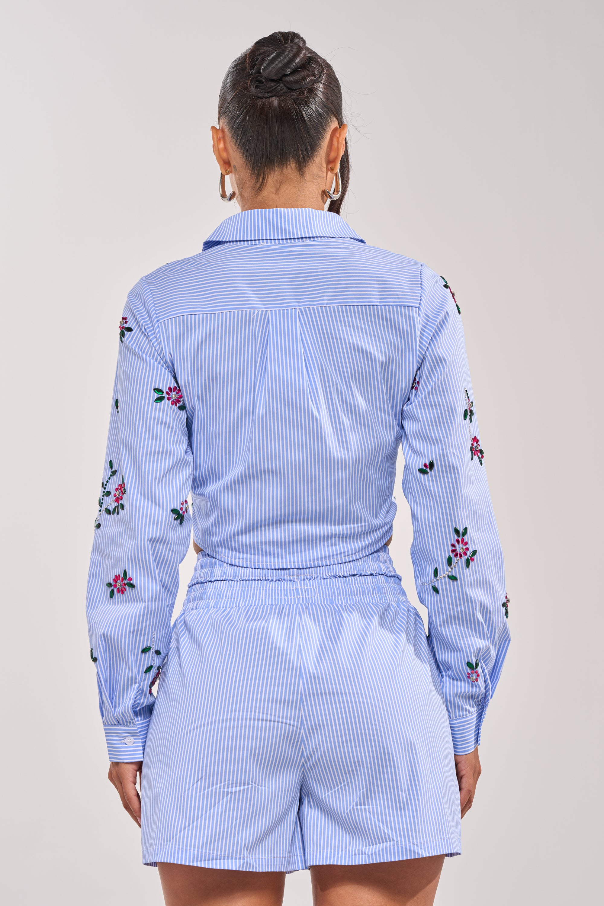 A woman stands facing away, wearing the JUNIE POPLIN RHINESTONE DETAIL BLOUSE with her hair pulled back and hoop earrings as accessories. 2