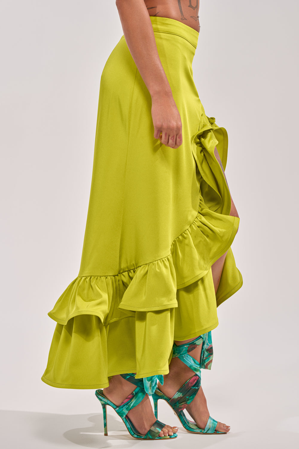 A person models the LADY LUXE RUCHED MIDI SKIRT WITH HIGH SLIT in bright chartreuse, styled with teal and green strappy high-heeled sandals, standing against a plain light background. 4