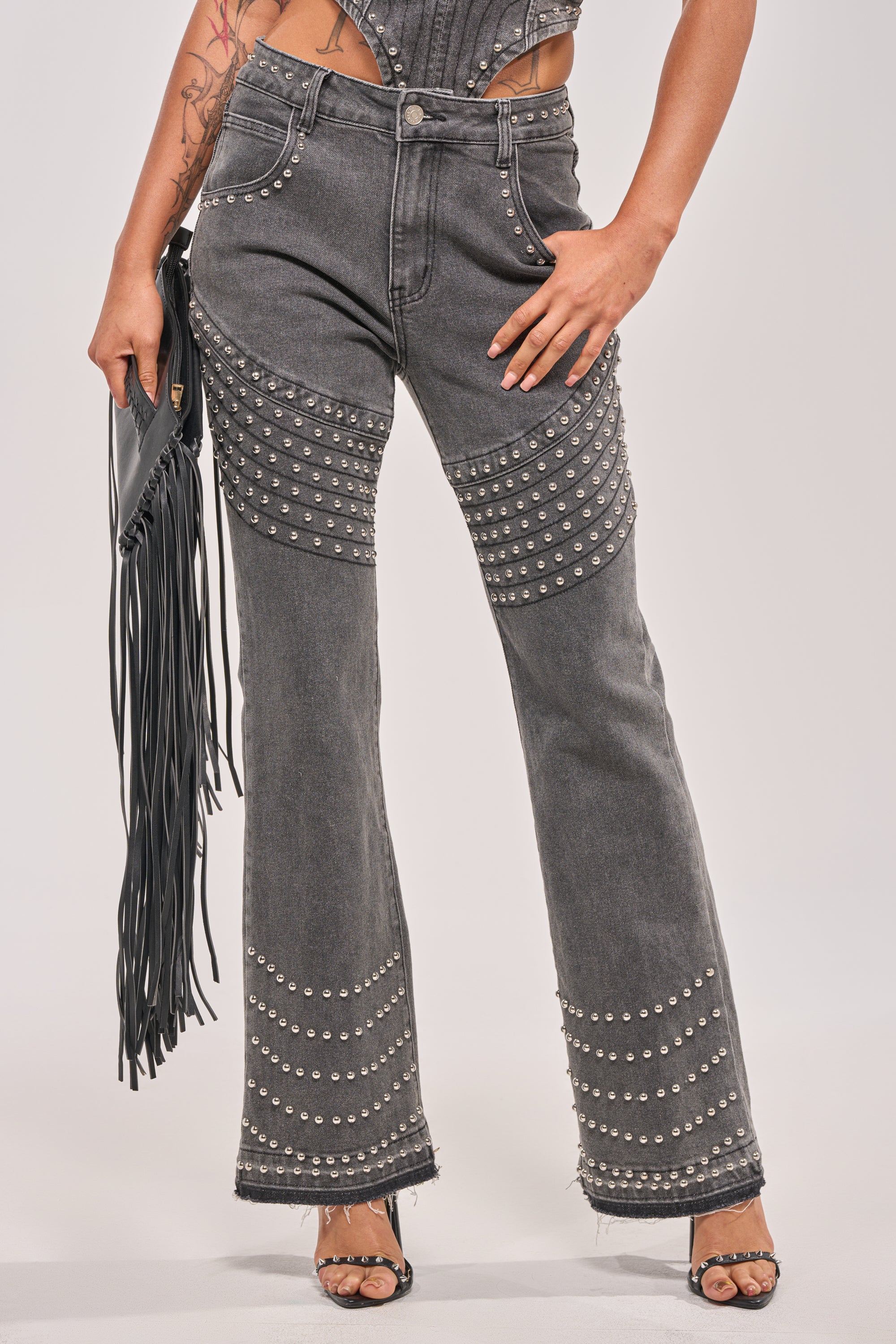 Wearing FEELING THE VIBES FLARE DENIM in high-waisted dark gray, styled with a black fringed clutch and black heeled sandals. The look highlights the lower body, creating a sleek, rocker-chic vibe. 1