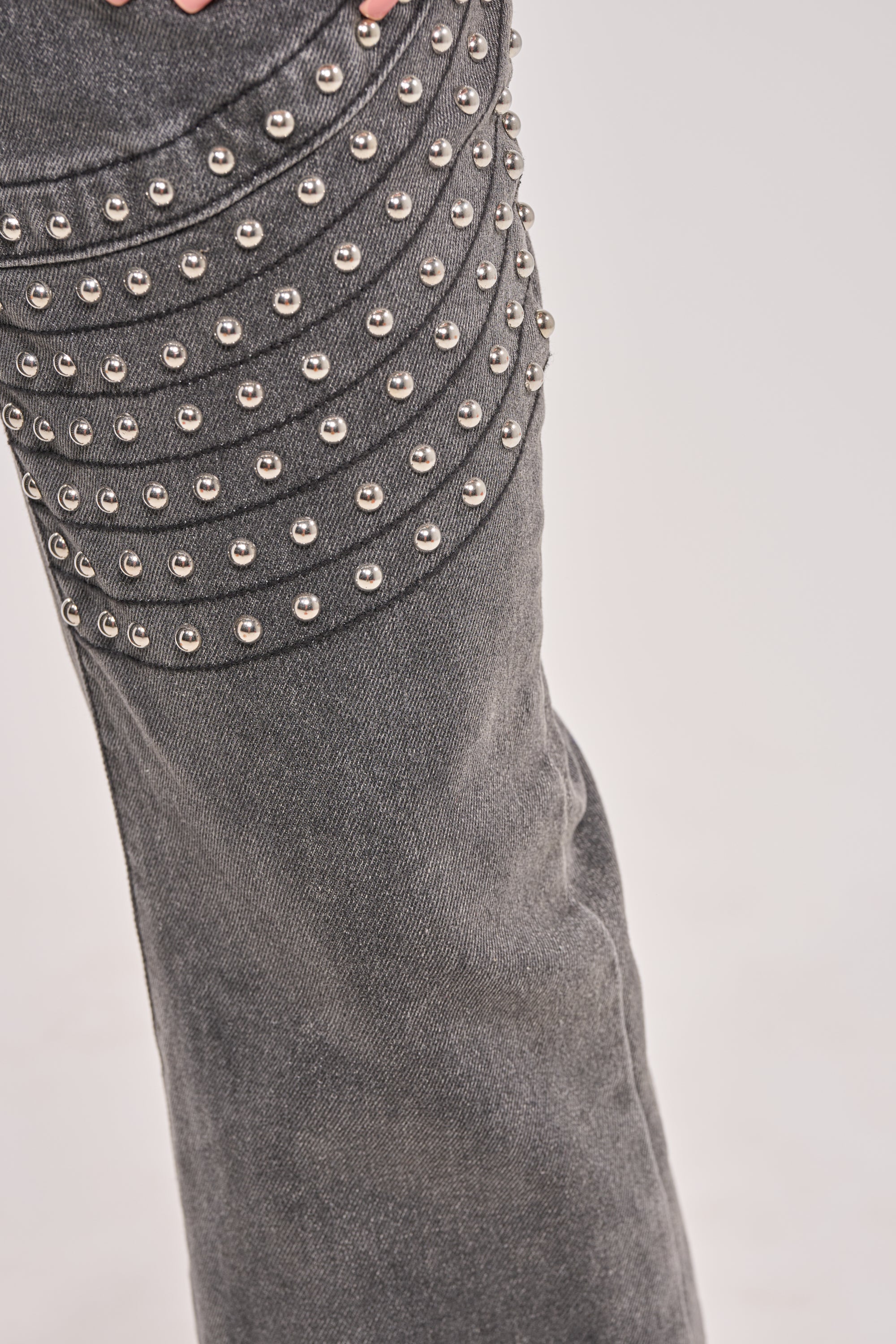 Close-up of the FEELING THE VIBES FLARE DENIM shows a grey pant leg with dome stud accents arranged in horizontal rows near the knee, forming a stylish textured pattern against a plain light background. 4