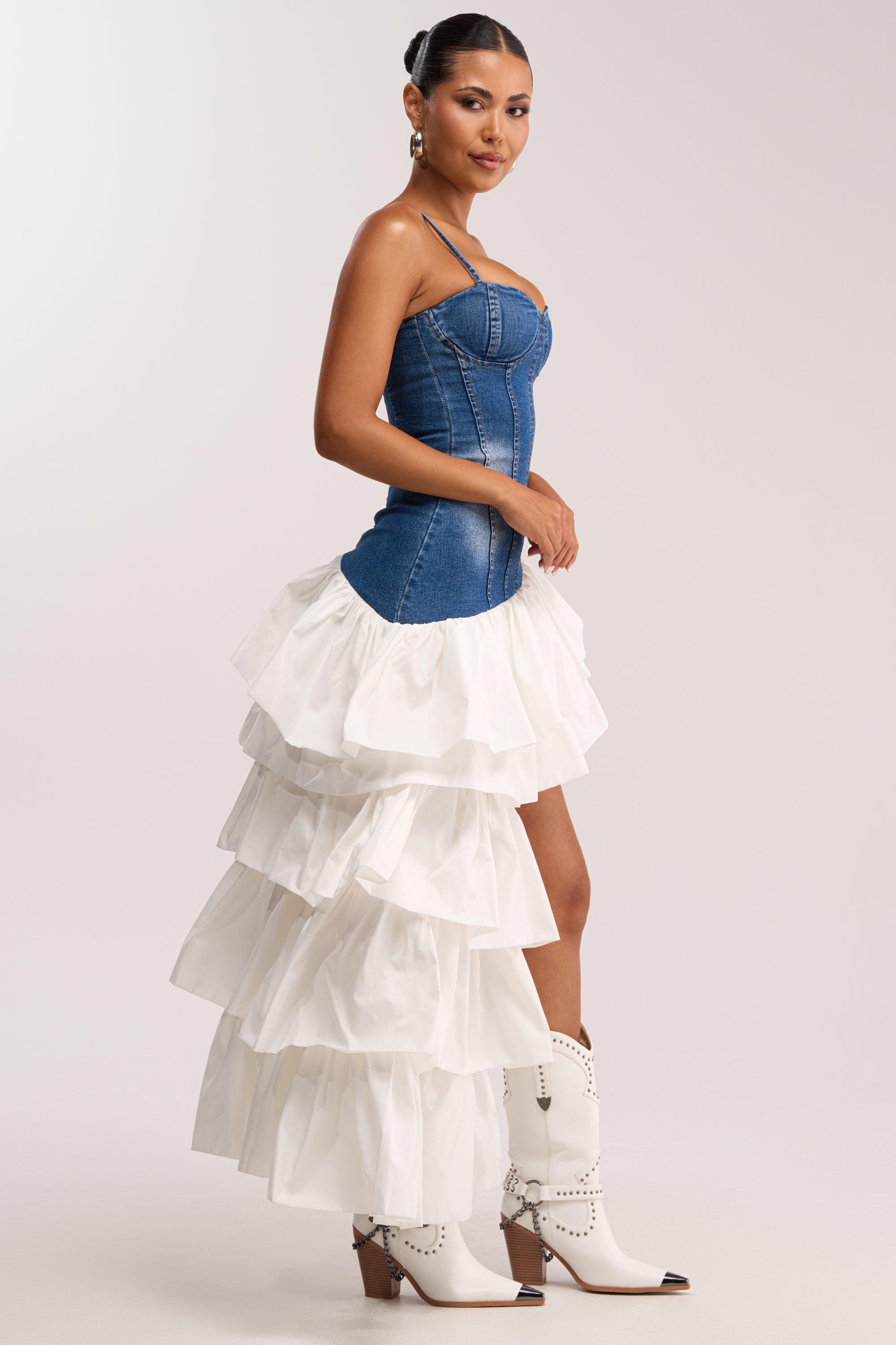 A woman models the WEB CRUSH MAXI DRESS IN DARK DENIM with white cowboy boots against a plain light background.