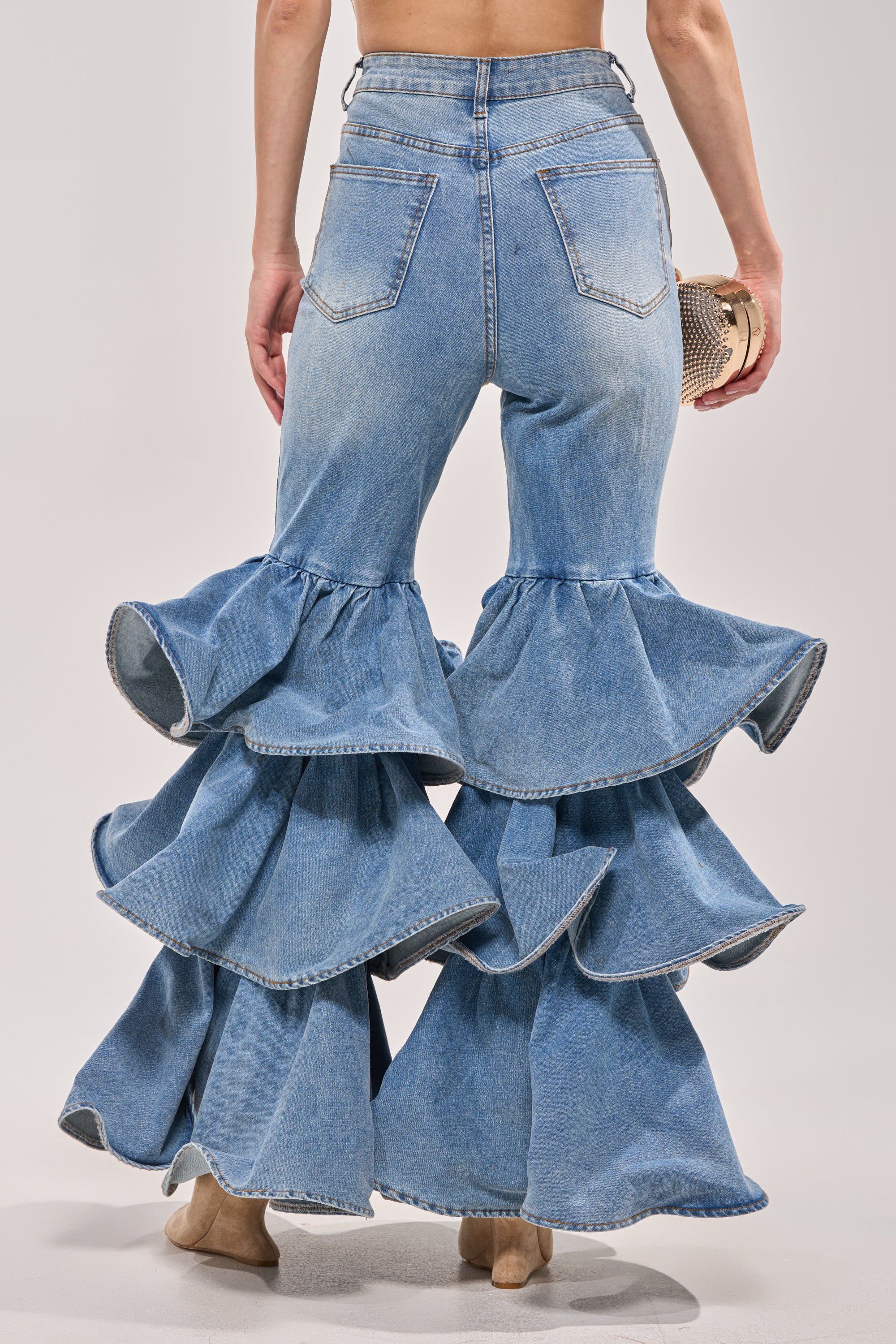 Wearing RUFFLE CITY DENIM high-rise stretch jeans with dramatic ruffle flares from mid-thigh, styled with nude heels and a small round clutch for a bold, western-inspired look. 4