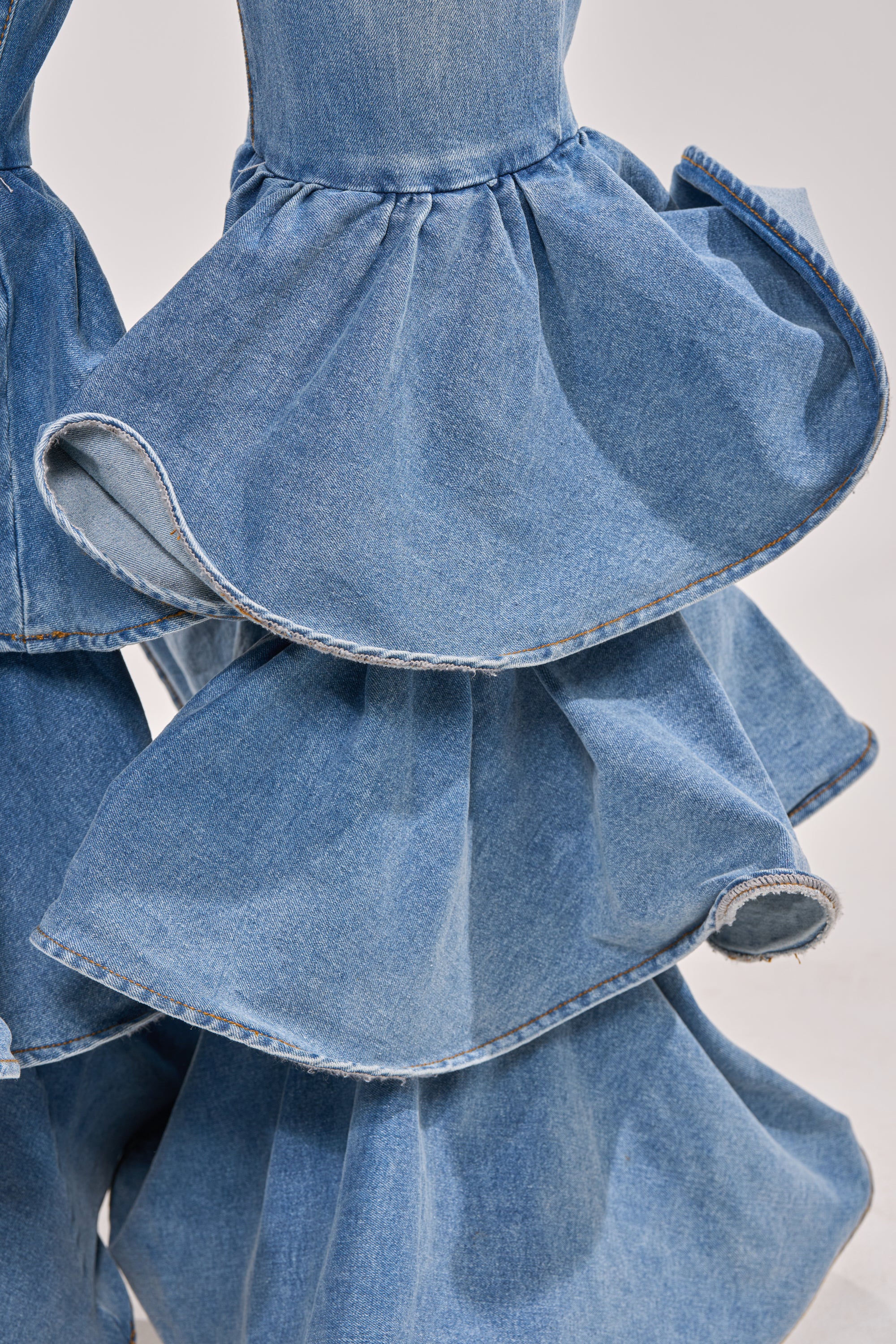 Close-up of RUFFLE CITY DENIM: high-rise stretch jeans featuring dramatic, tiered ruffle flares with layered, wavy fabric details for a bold, western-inspired look. 6