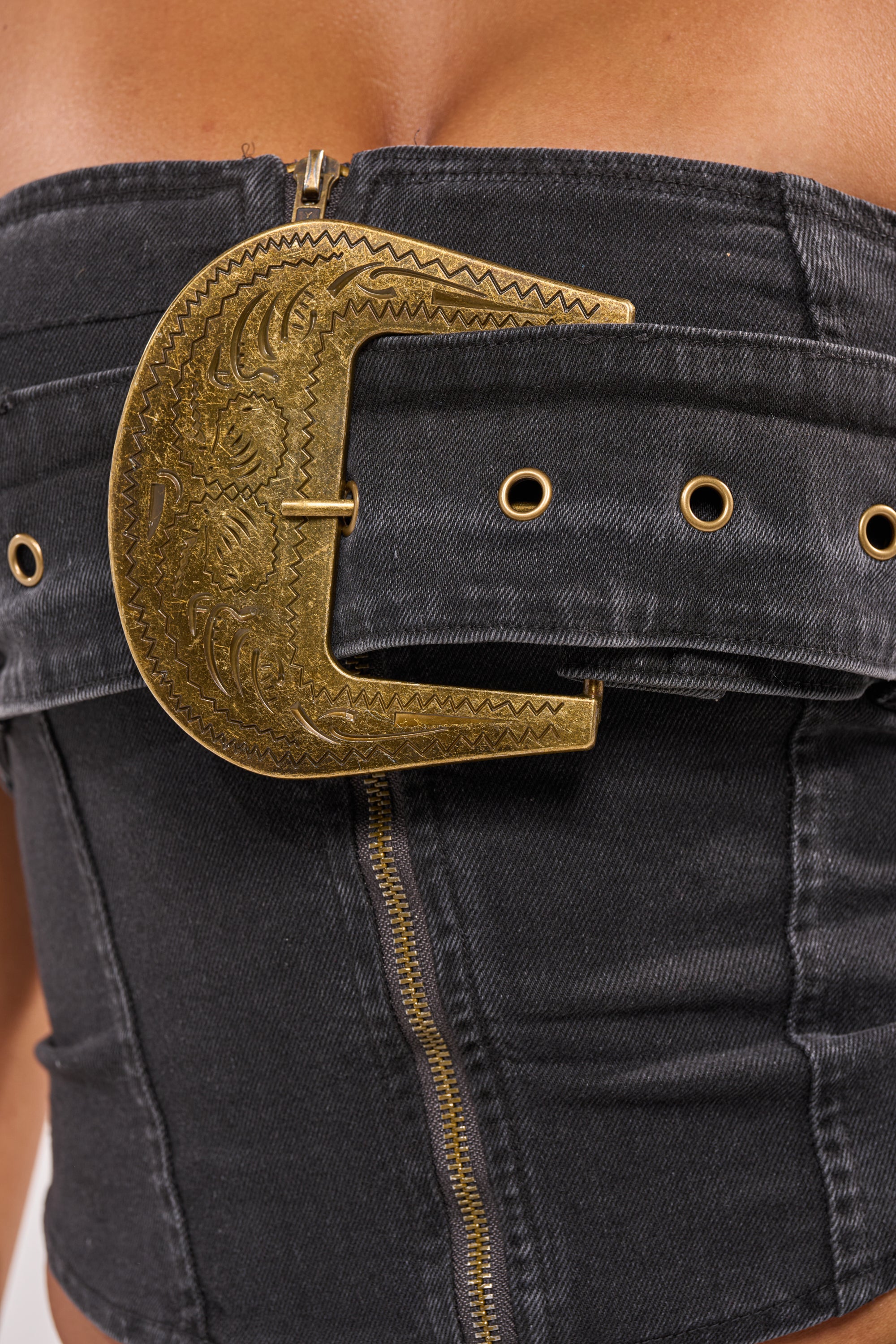 Close-up of the BUCKIN DENIM TUBE TOP, a black denim corset-style tube top with gold grommets, a front gold zipper, and a bold western-inspired ornate belt buckle—perfect for making a statement on your next night out. 6