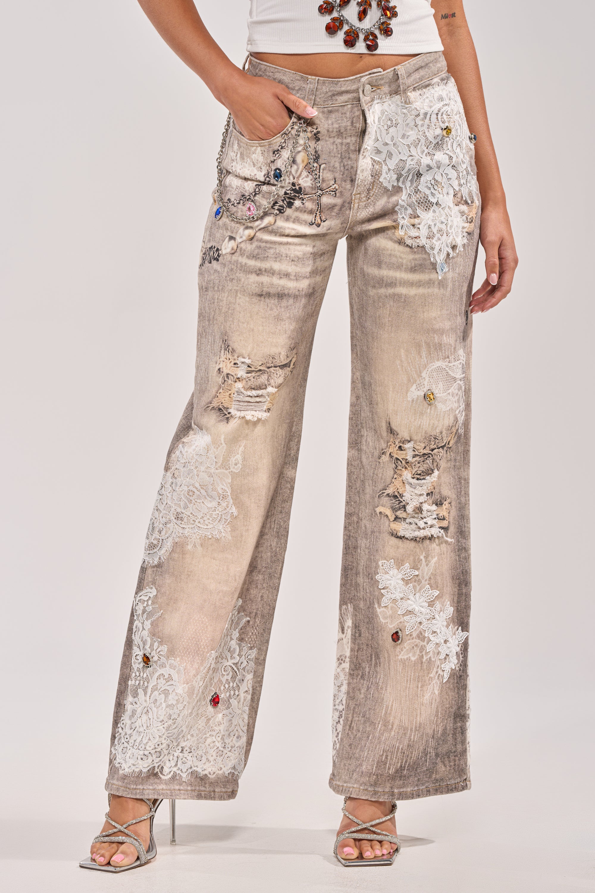 Someone wearing the DONT MESS WITH ME RELAXED DENIM—wide-legged jeans with lace details and colorful jeweled accents—styled with a white tank top and silver high-heeled sandals. 1