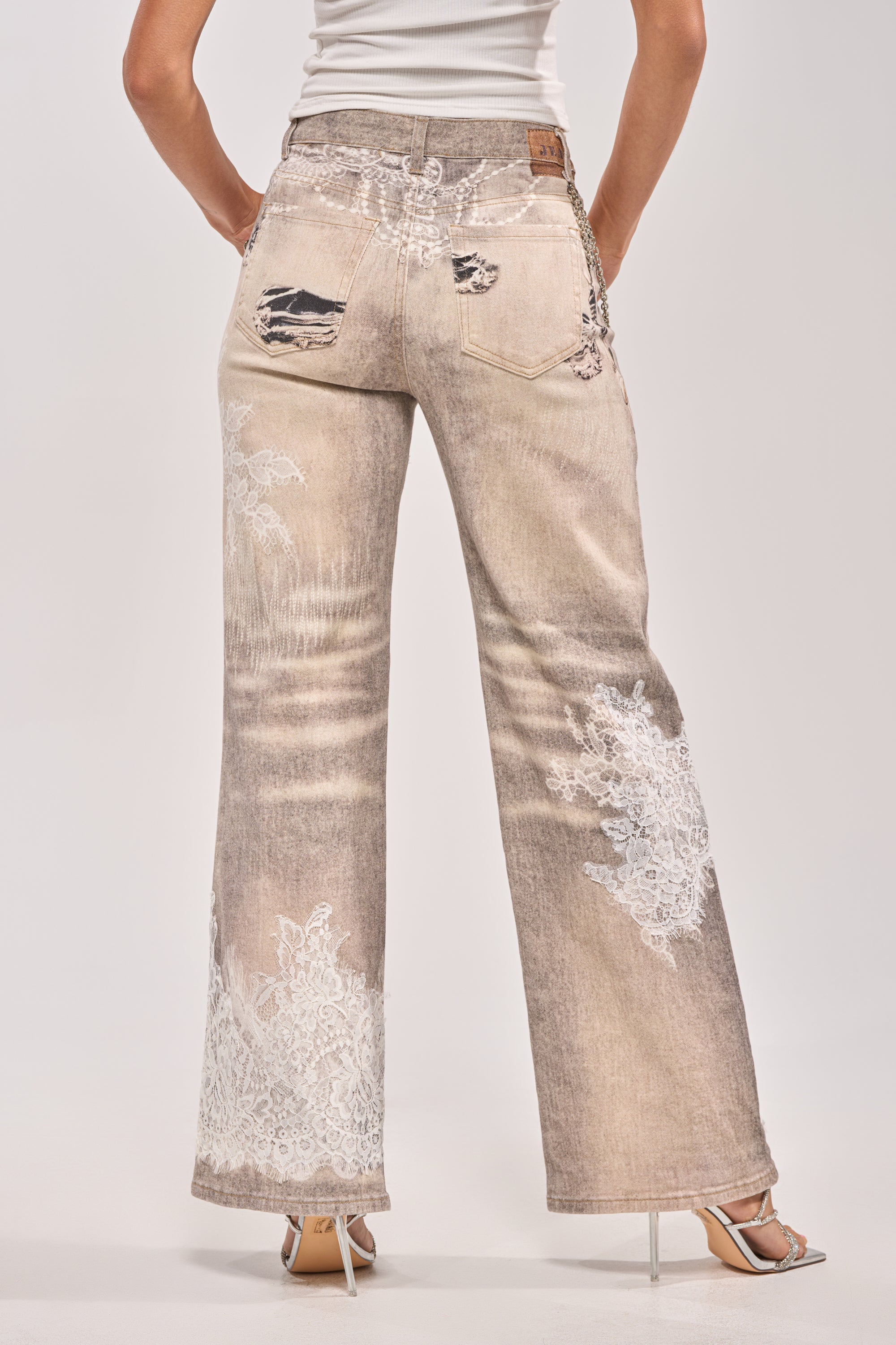 A person faces away, wearing the DONT MESS WITH ME RELAXED DENIM—lace embellished, wide-leg distressed jeans—paired with a white sleeveless top and heeled sandals against a plain background. 4