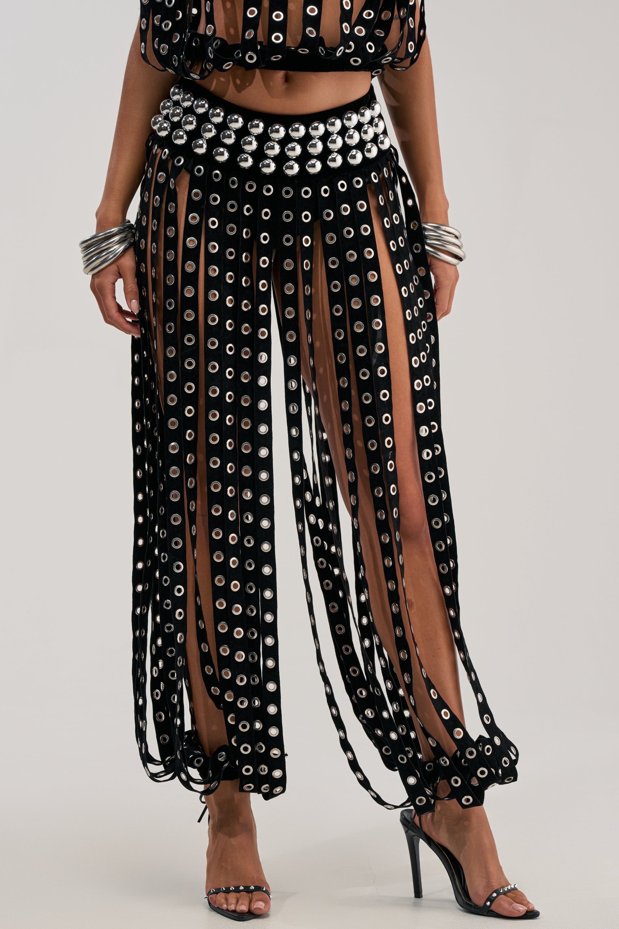 Someone wearing TOUCH IT GROMMET JOGGER features rocker chic style with black sheer panels, vertical strips, a matching waistband, silver bracelets, and black high-heeled sandals, showing their midriff and lower legs.