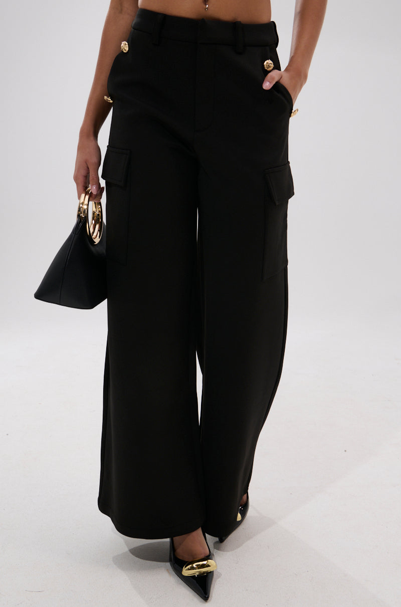 Wearing the chic GOTTA LET IT GO TROUSER, styled with cargo flap pockets, paired with a black gold-handle handbag and black pointed-toe heels featuring gold accents.