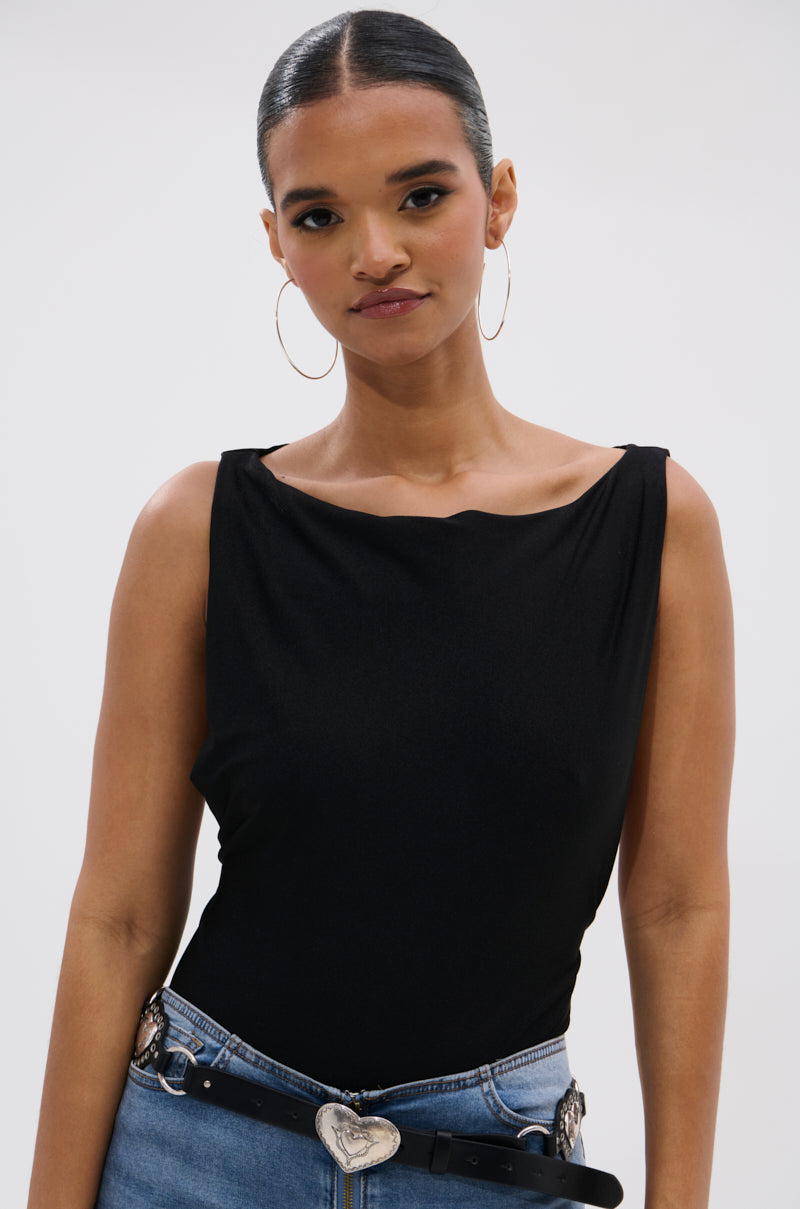 A woman with slicked-back hair and hoop earrings models the SEXY OPEN SIDE BODYSUIT with blue jeans and a black belt with a heart-shaped buckle, highlighting her curve-skimming silhouette against a plain light background.